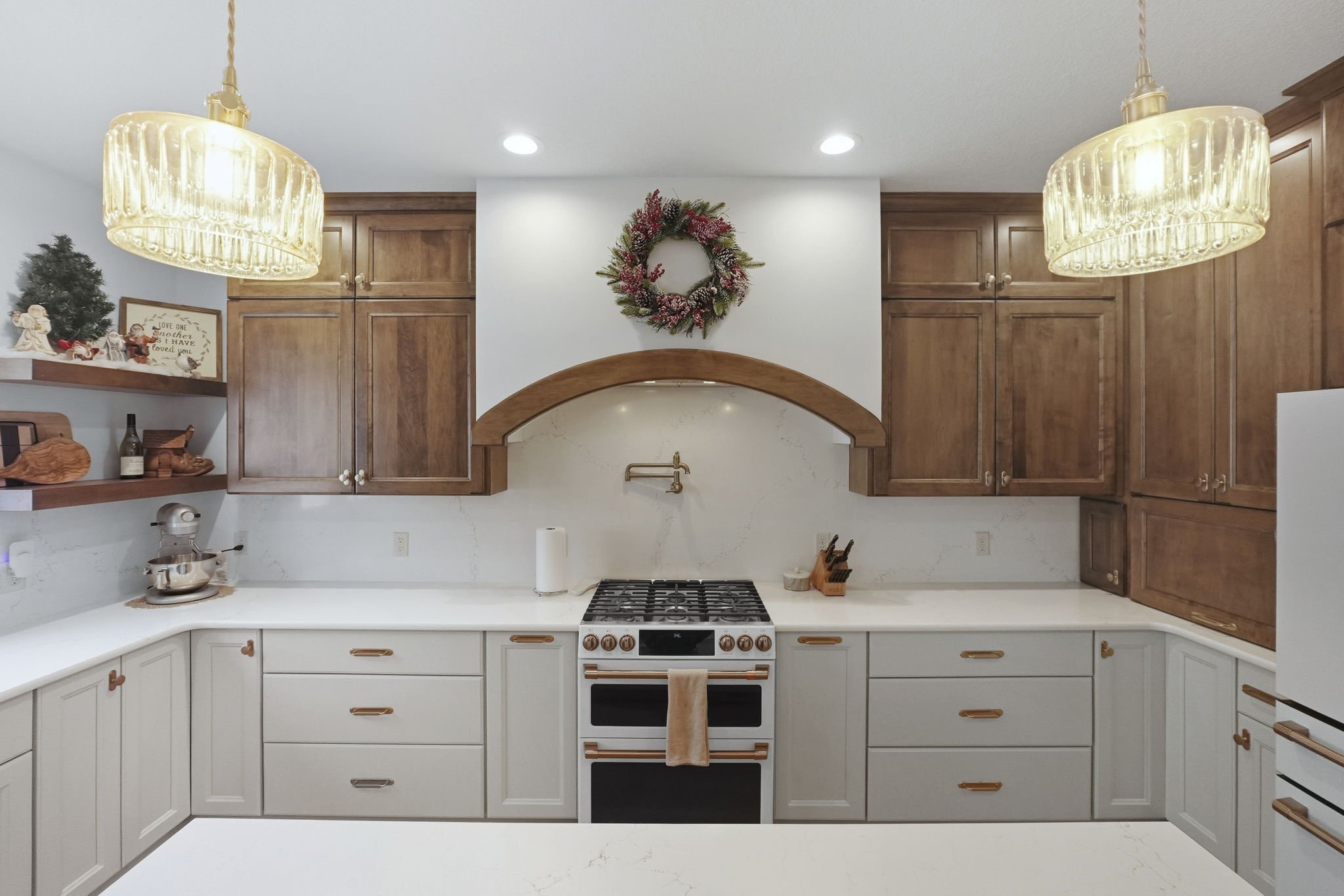 Kitchen with wooden upper cabinets, white lower cabinets, a white marble backsplash, a white stove with a towel hanging, Christmas wreath above, and two hanging pendant lights.