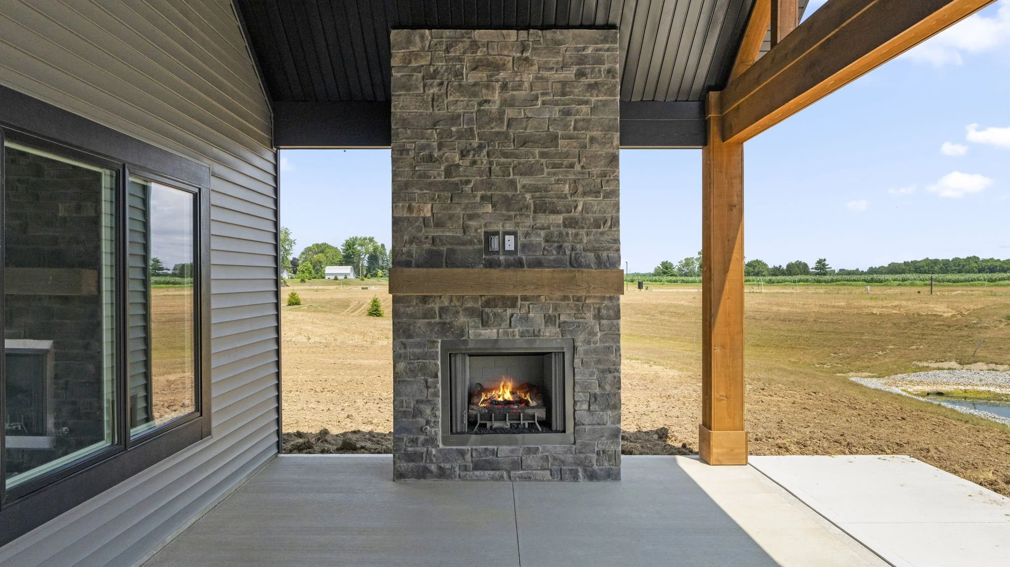 Covered porch with a fireplace, brick chimney, and panoramic view of open land and trees.
