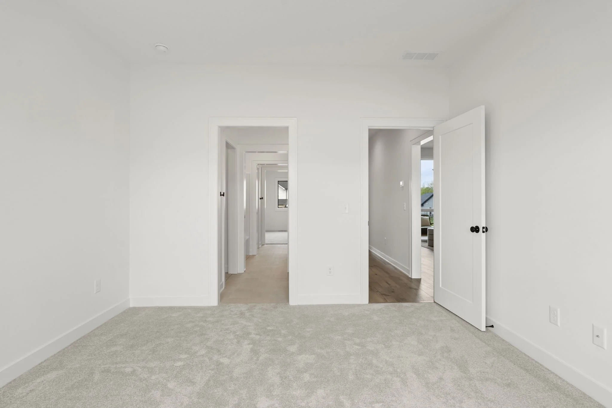 Empty room with beige carpet and white walls, with multiple doorways leading to hallways and other rooms.