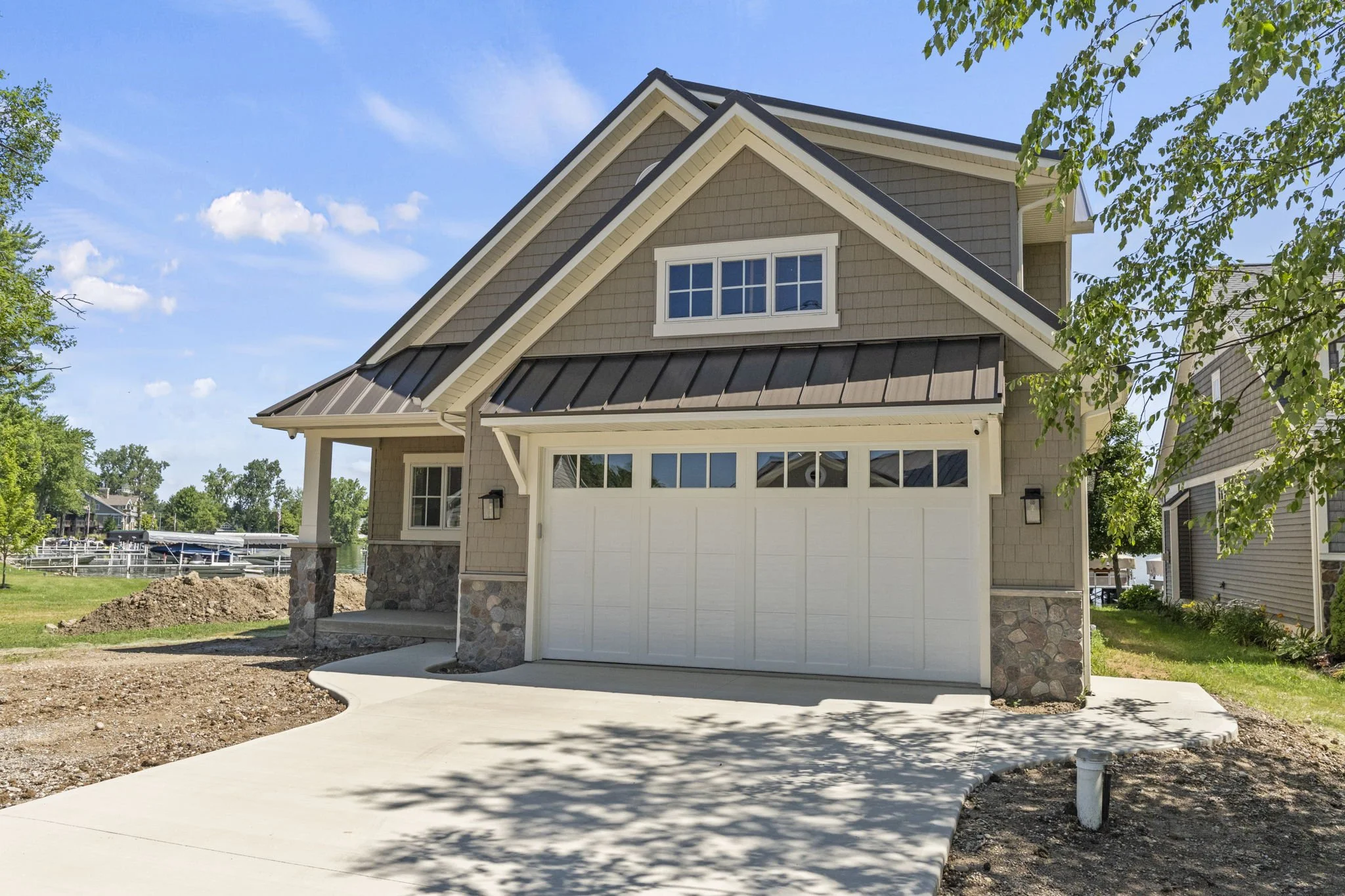 Newly constructed house with a two-car garage, beige siding, stone accents, and a landscaped yard on a sunny day.