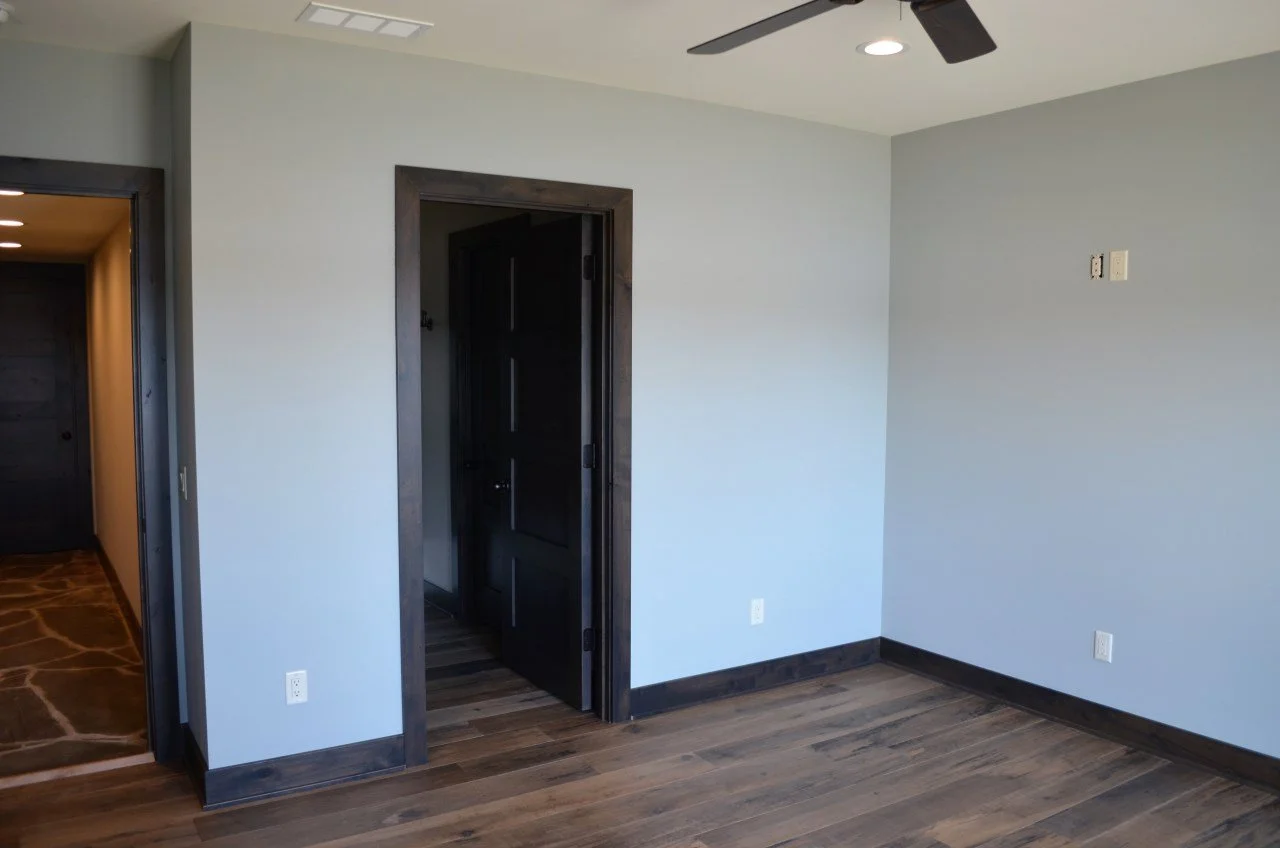 Empty room with hardwood floors, white and gray walls, and dark wood trim around doorways. A ceiling fan and recessed lighting are visible. There are visible electrical outlets and a wall-mounted network connection.