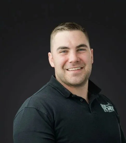A smiling man with short brown hair, wearing a black polo shirt, against a black background.