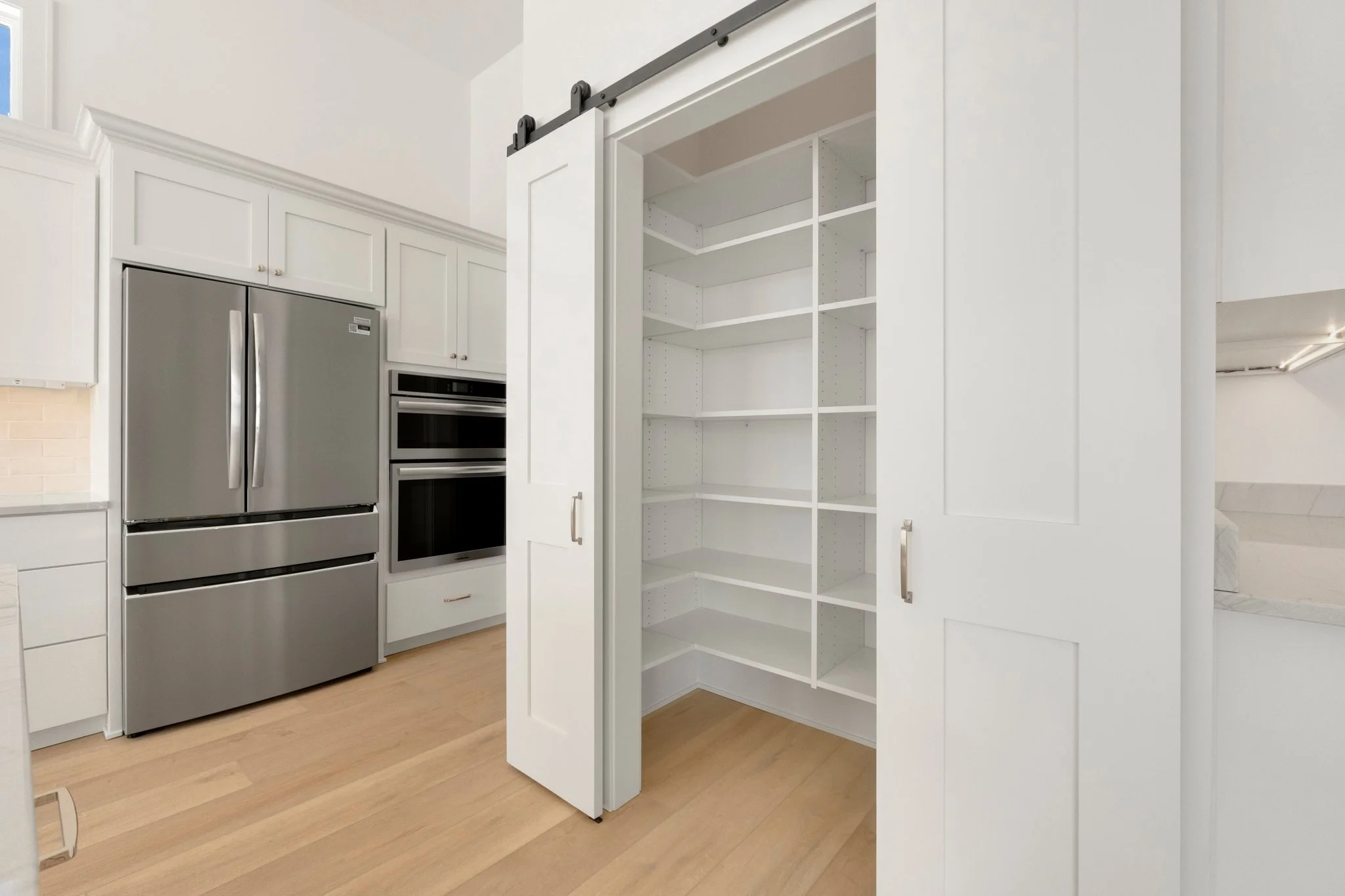 Empty white pantry with sliding doors in a modern kitchen.