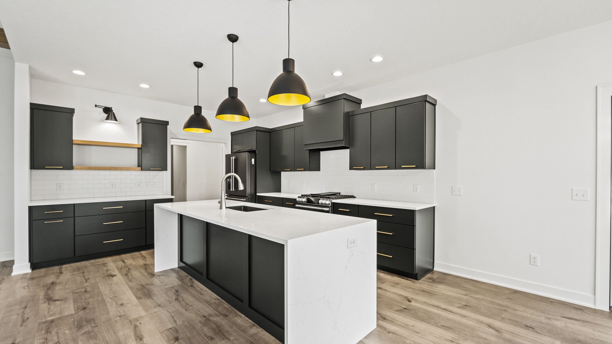 Modern kitchen with black cabinets, white countertop island, stainless steel appliances, black pendant lights with yellow interior, and white subway tile backsplash.