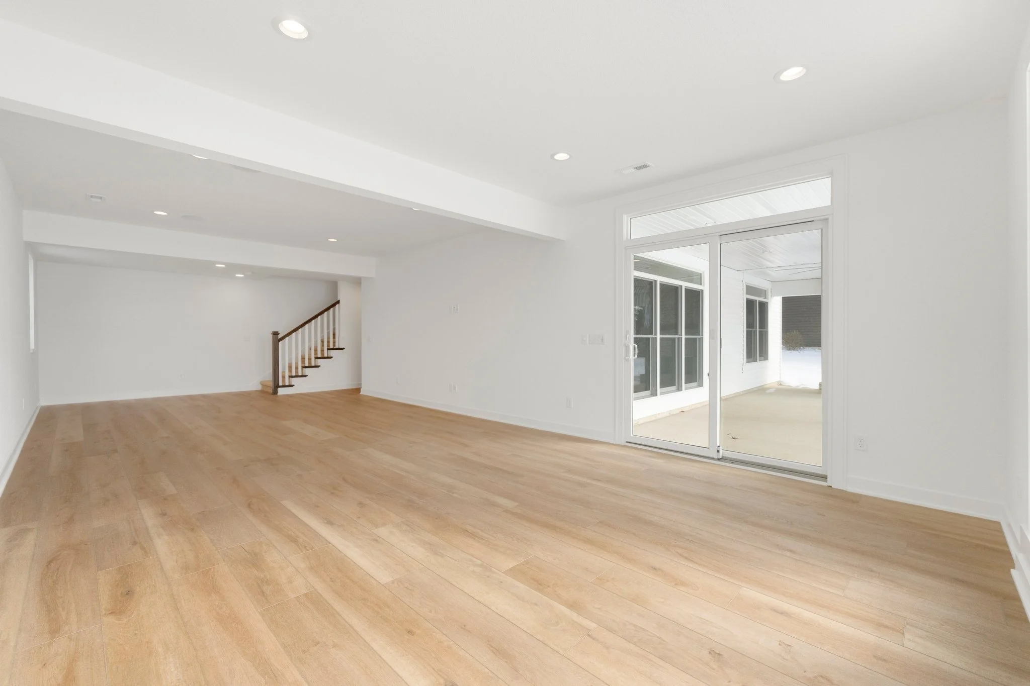 Empty living room with light wood flooring, white walls, and large sliding glass door leading to a porch.