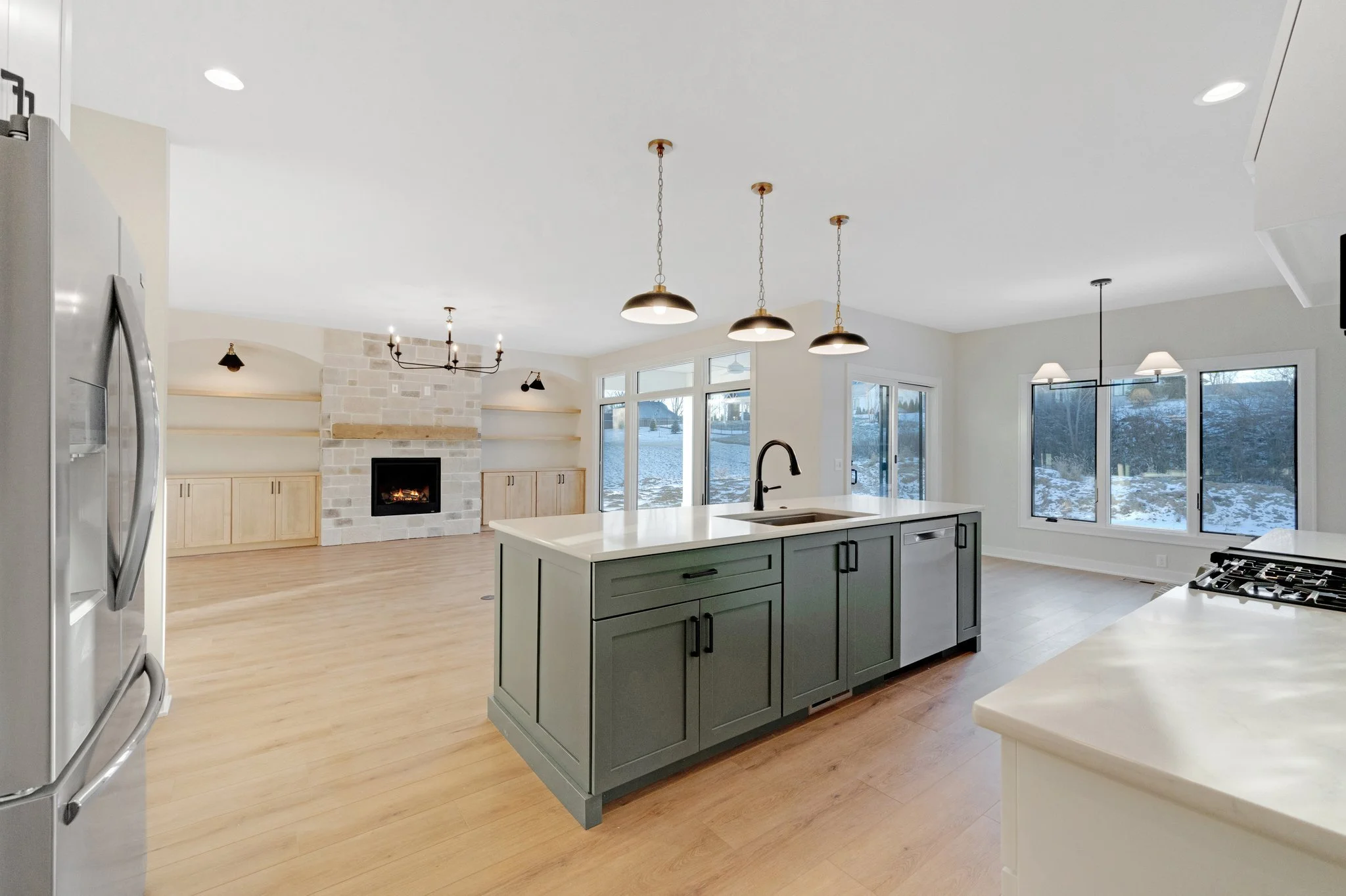 Open-concept kitchen and living room with large windows, central island, and fireplace.