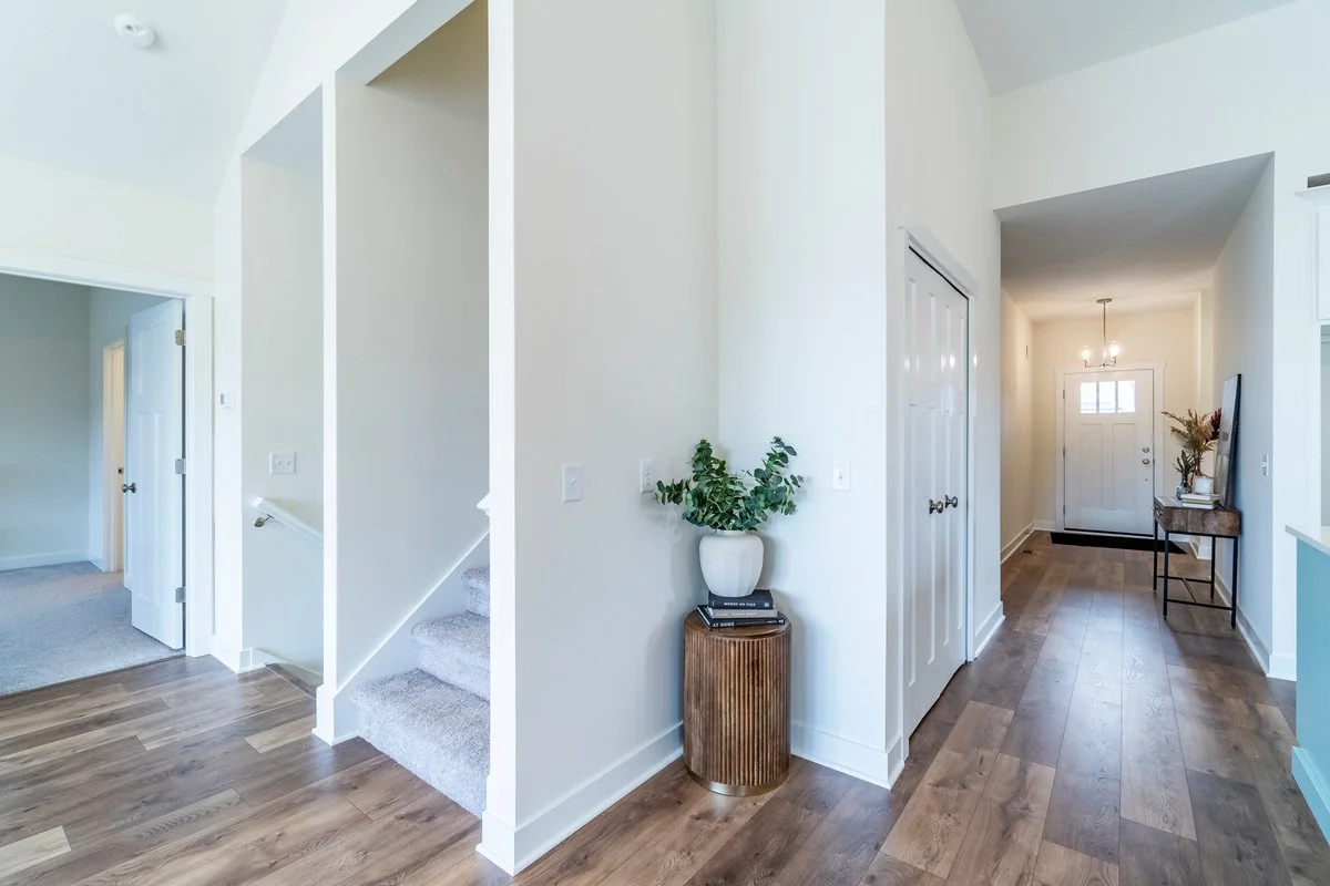 Hallway in a modern home with wooden flooring, white walls, a staircase, and a small table with a potted plant