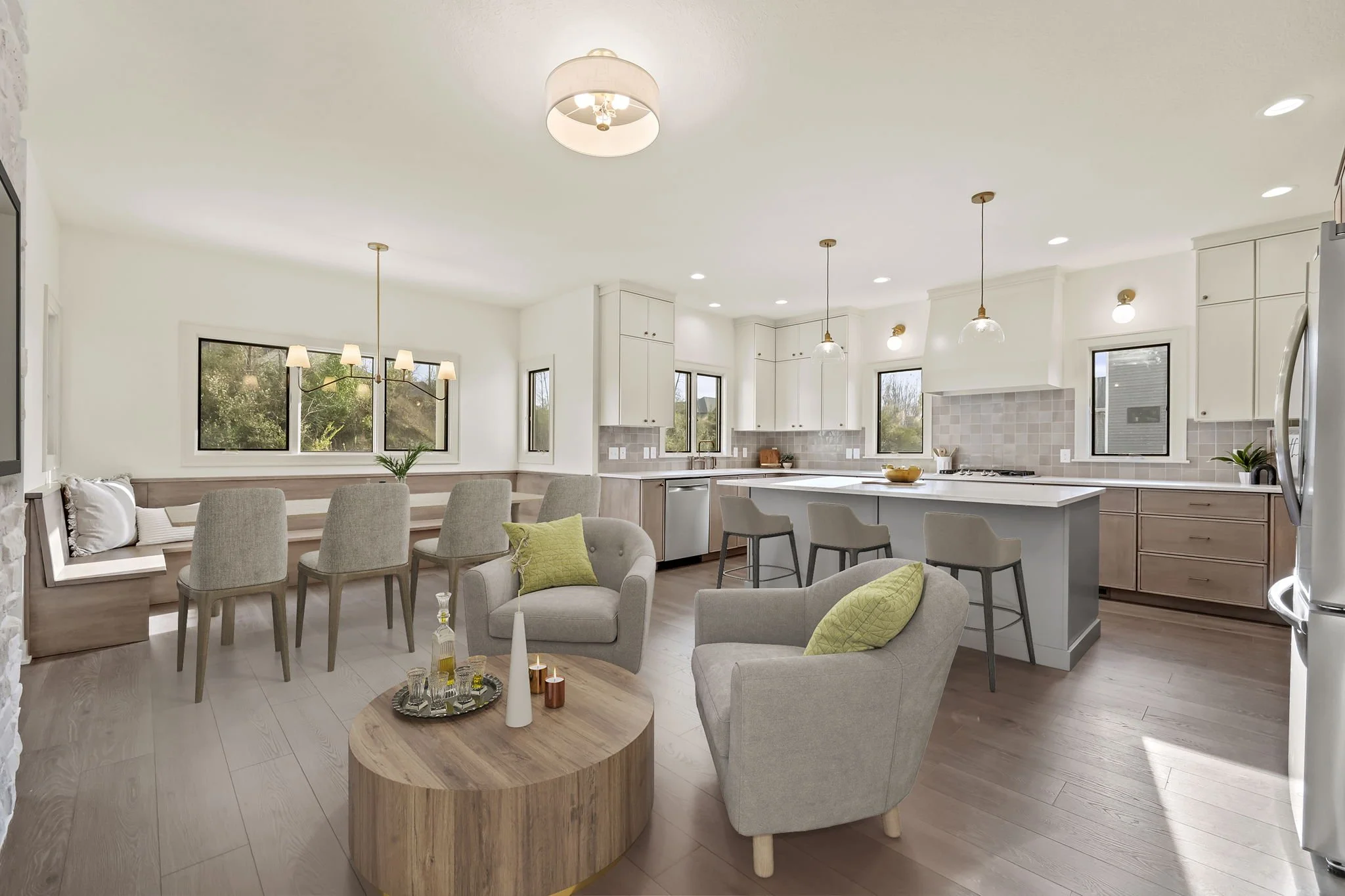 Open-concept living space with a kitchen and dining area, featuring white cabinetry, a large island with bar stools, and a seating area with two armchairs and a round wooden coffee table.
