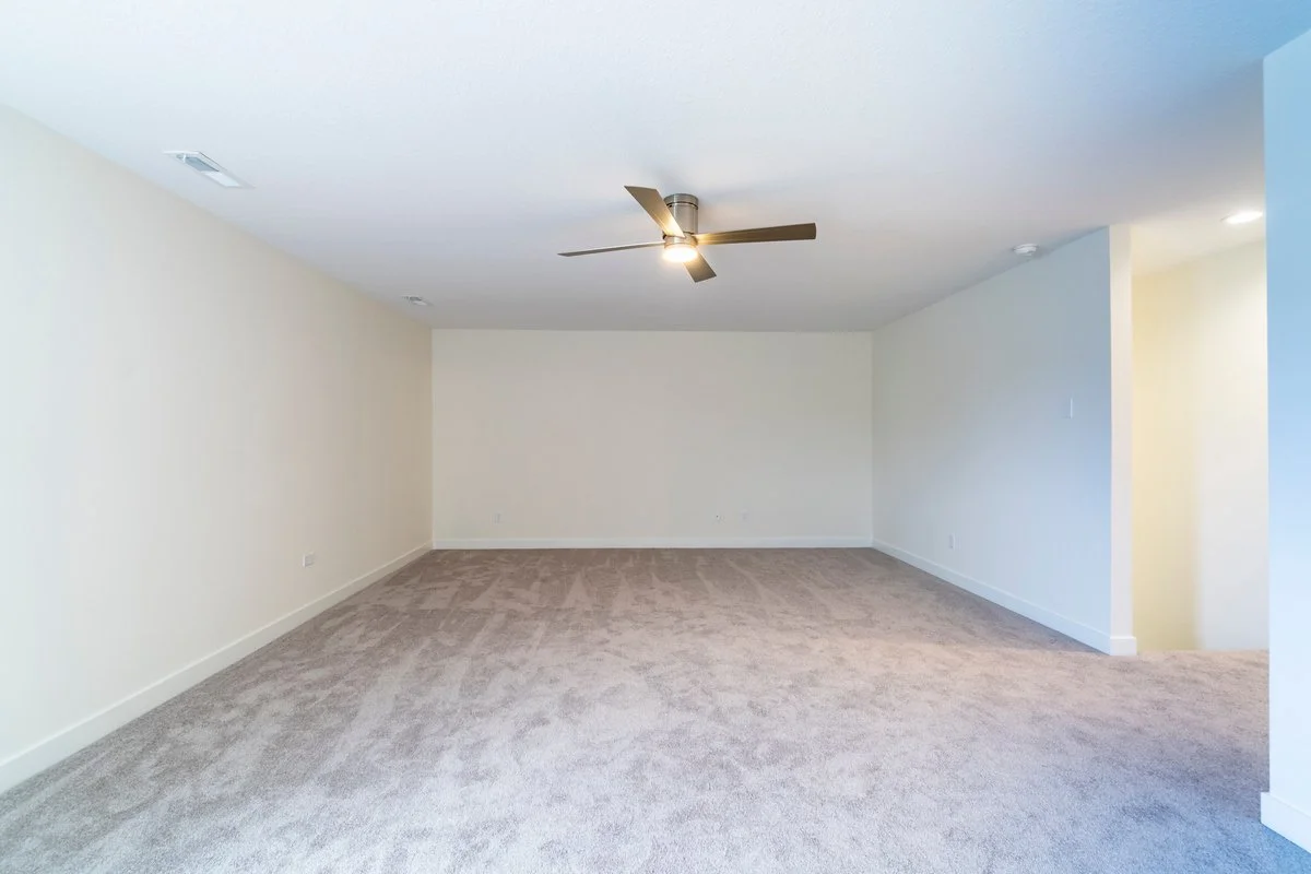 Empty living room with beige walls, a ceiling fan, and beige carpet flooring.