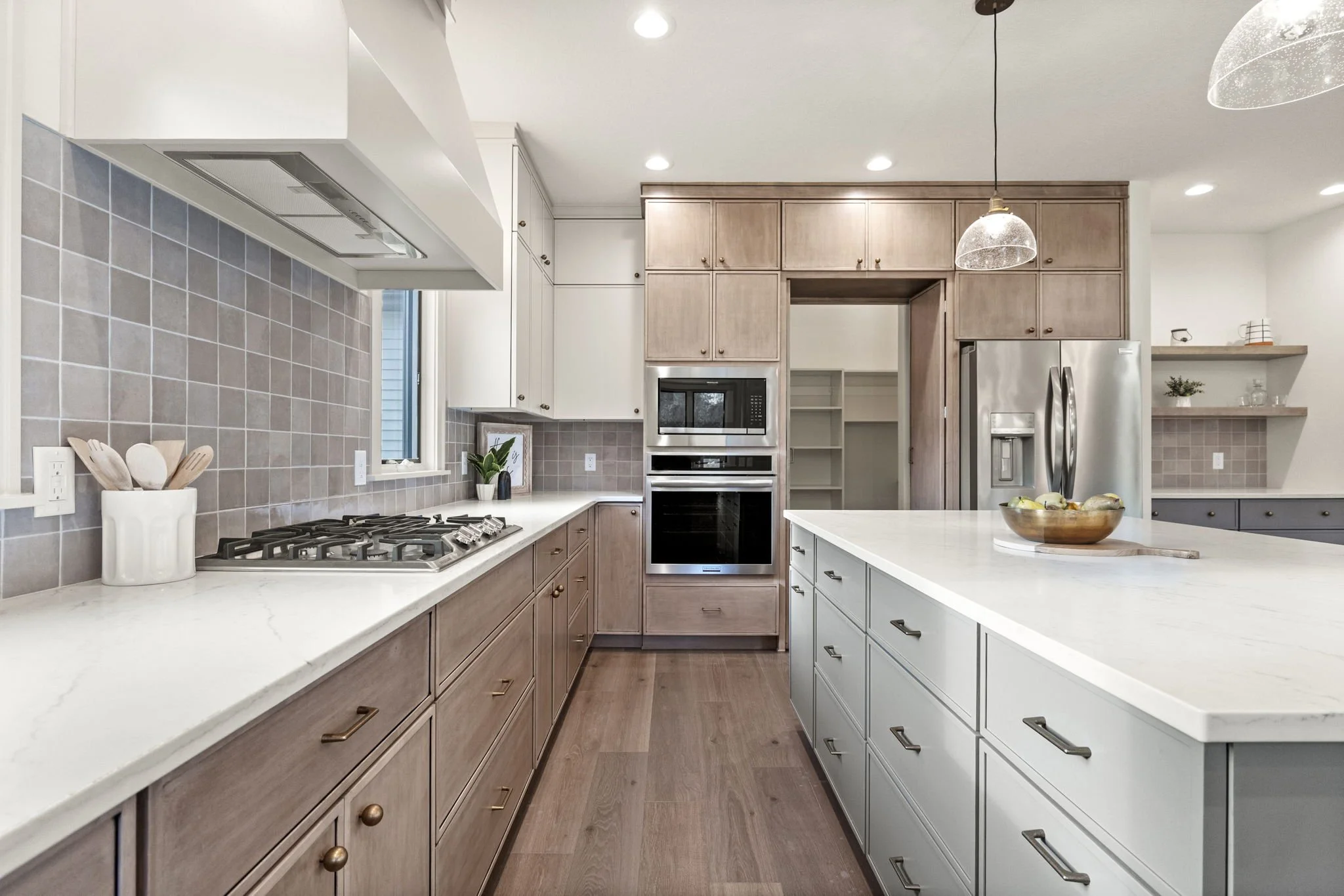 Modern kitchen with light wood and white cabinets, a large white island, stainless steel appliances, and a tiled backsplash.