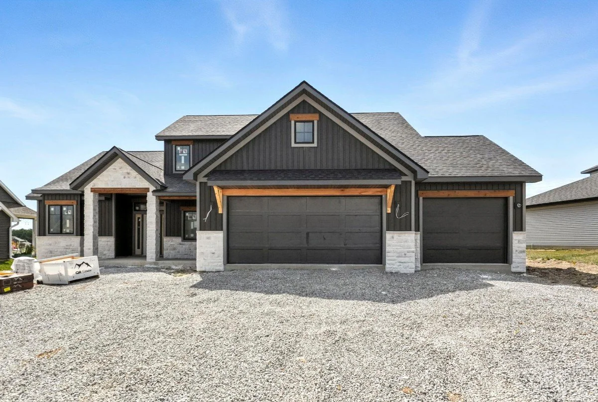 Newly constructed modern house with black and white exterior, three garage doors, gravel driveway, and blue sky.