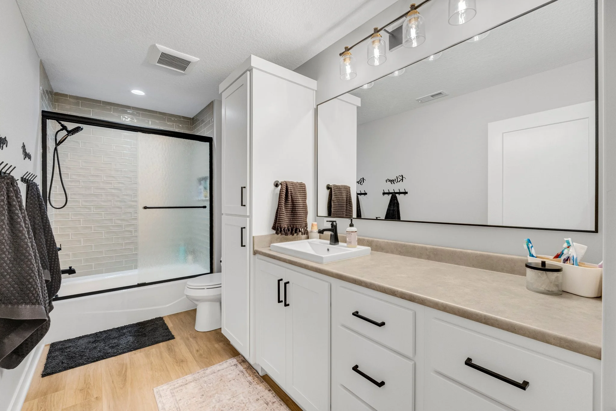 Modern bathroom with a large mirror, white cabinetry, a beige countertop, a shower with frosted glass door, and a toilet.