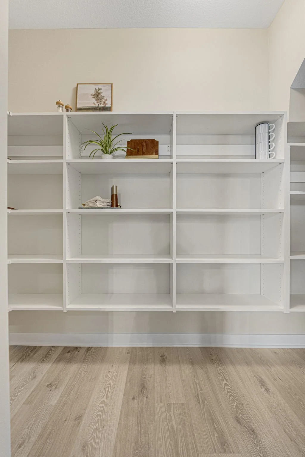 Empty white shelving unit with minimal decorative items, set against a light-colored wall and wooden floor.