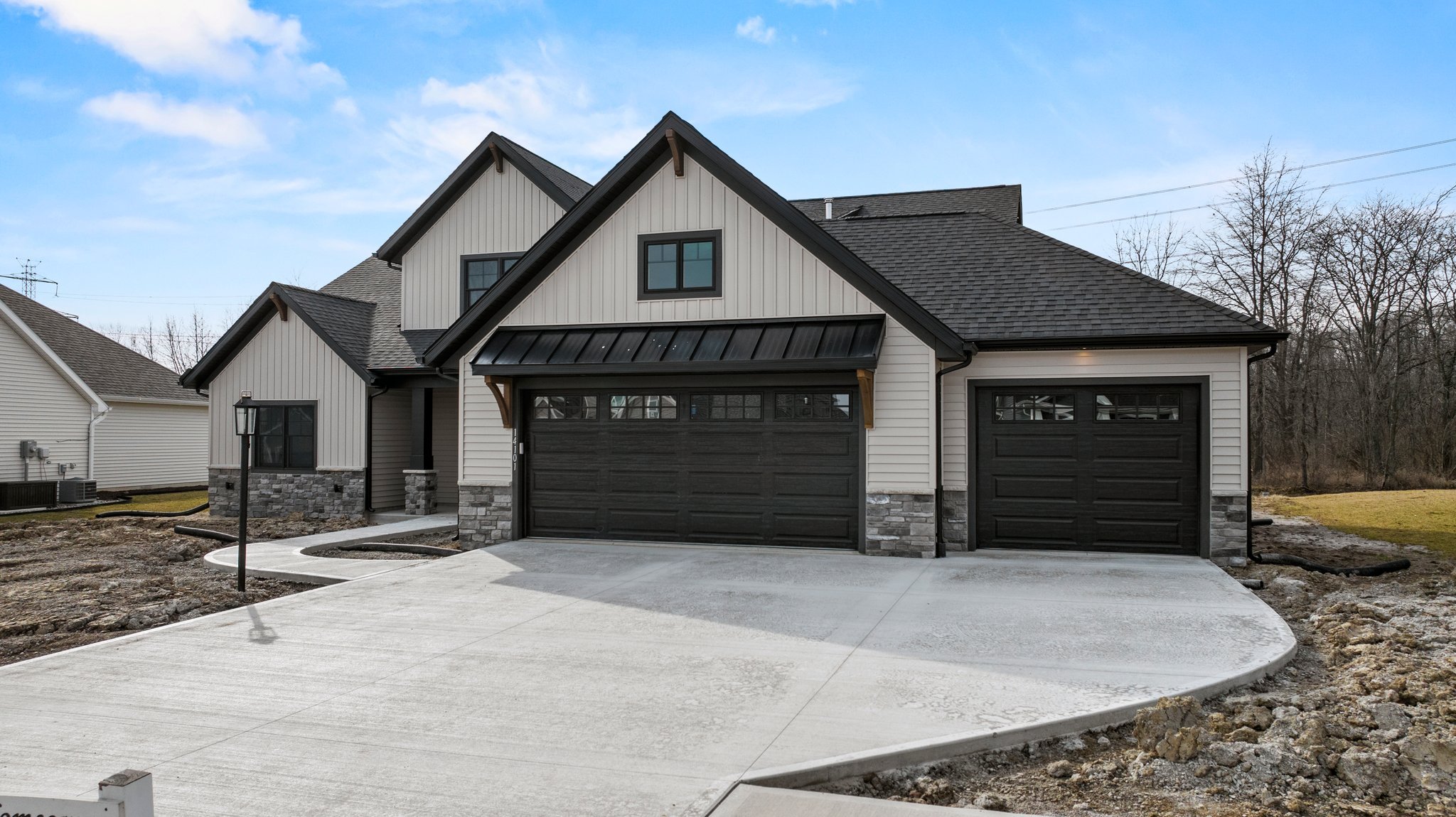 Newly built house with a black garage door, stone accents, and a black metal awning over the front entrance, with a concrete driveway and a lamp post in the front yard.