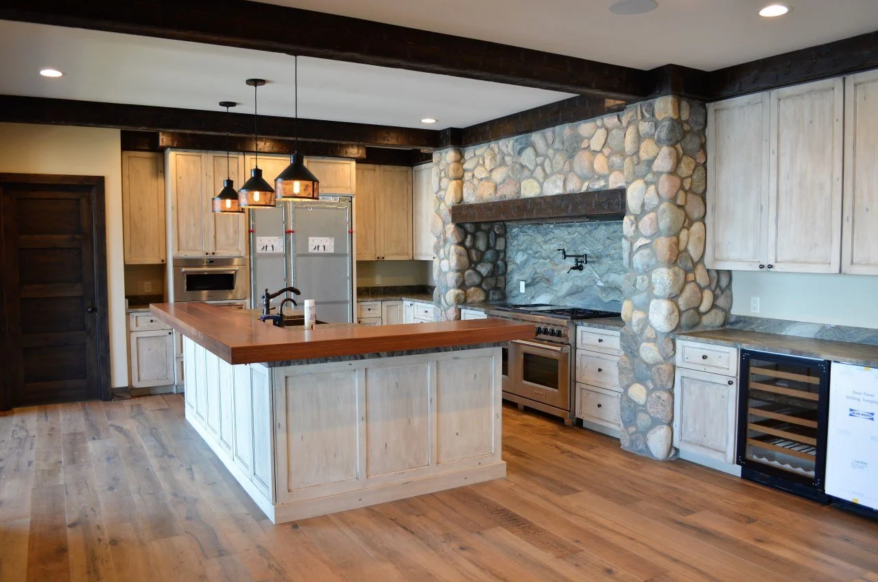 A spacious kitchen with a wooden island, light-colored cabinets, a stone accent wall surrounding the stove, and hardwood floors.