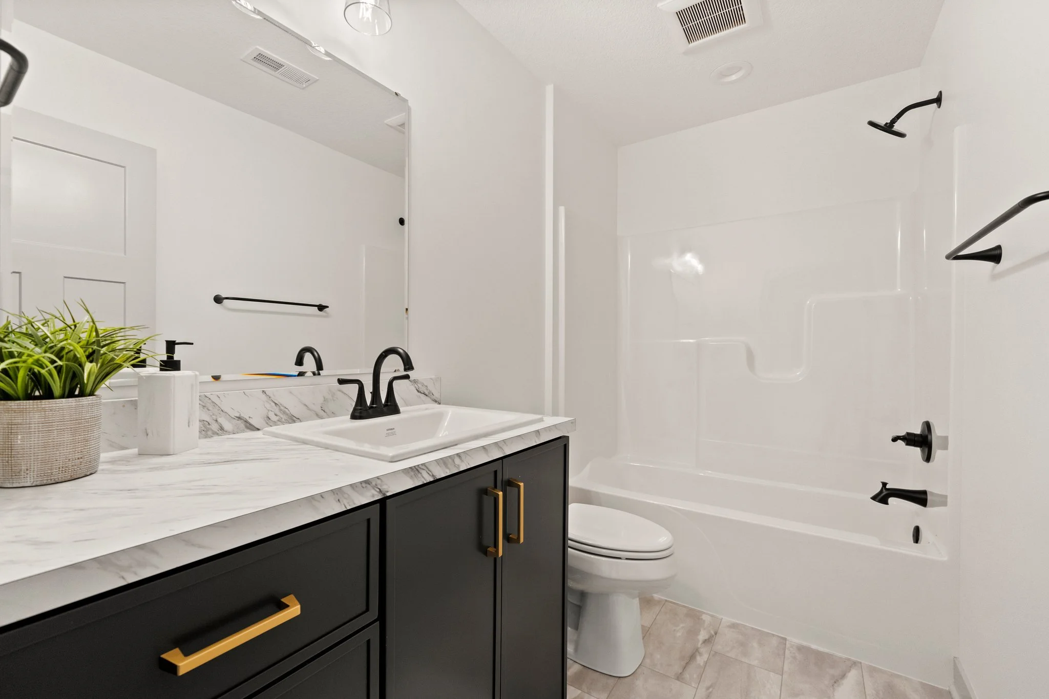 Modern bathroom with white walls, black fixtures, a marble countertop, a mirror, a plant, a sink, and a shower/tub combo.