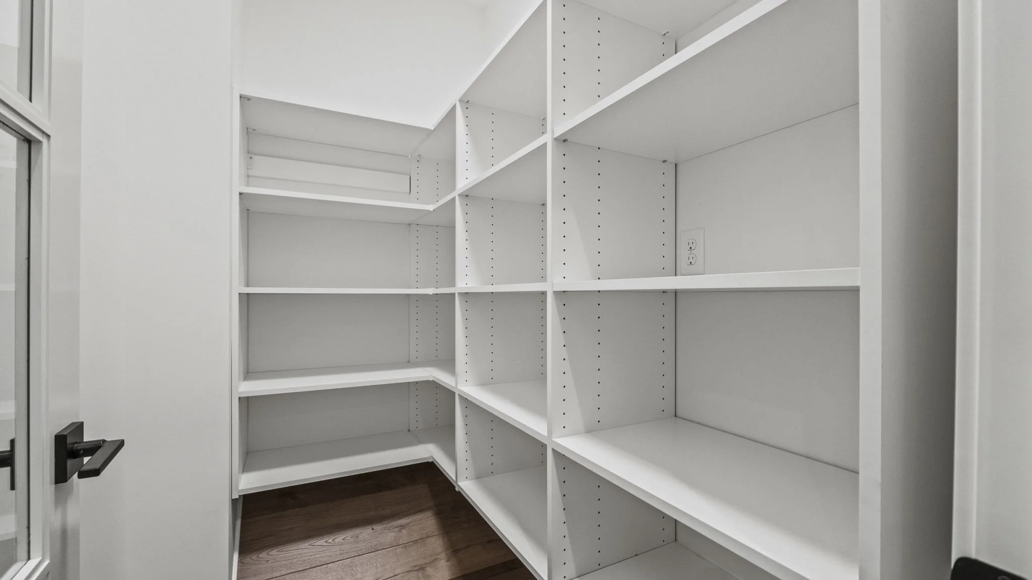 Empty white built-in pantry shelves in a small kitchen, with an electrical outlet on the wall.