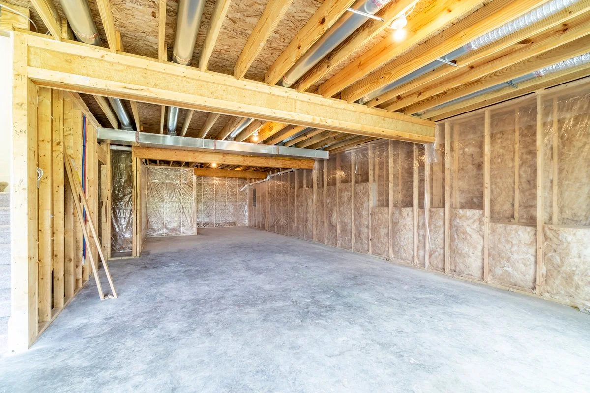 Empty garage with exposed wooden framing and insulation, concrete floor, and ductwork on ceiling.