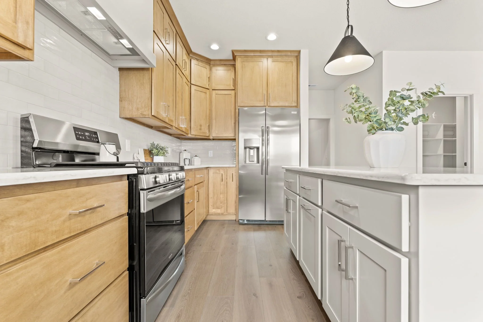 Kitchen with wooden cabinets, stainless steel refrigerator, black and stainless steel oven, white countertop, and a white island with a plant in a white vase.