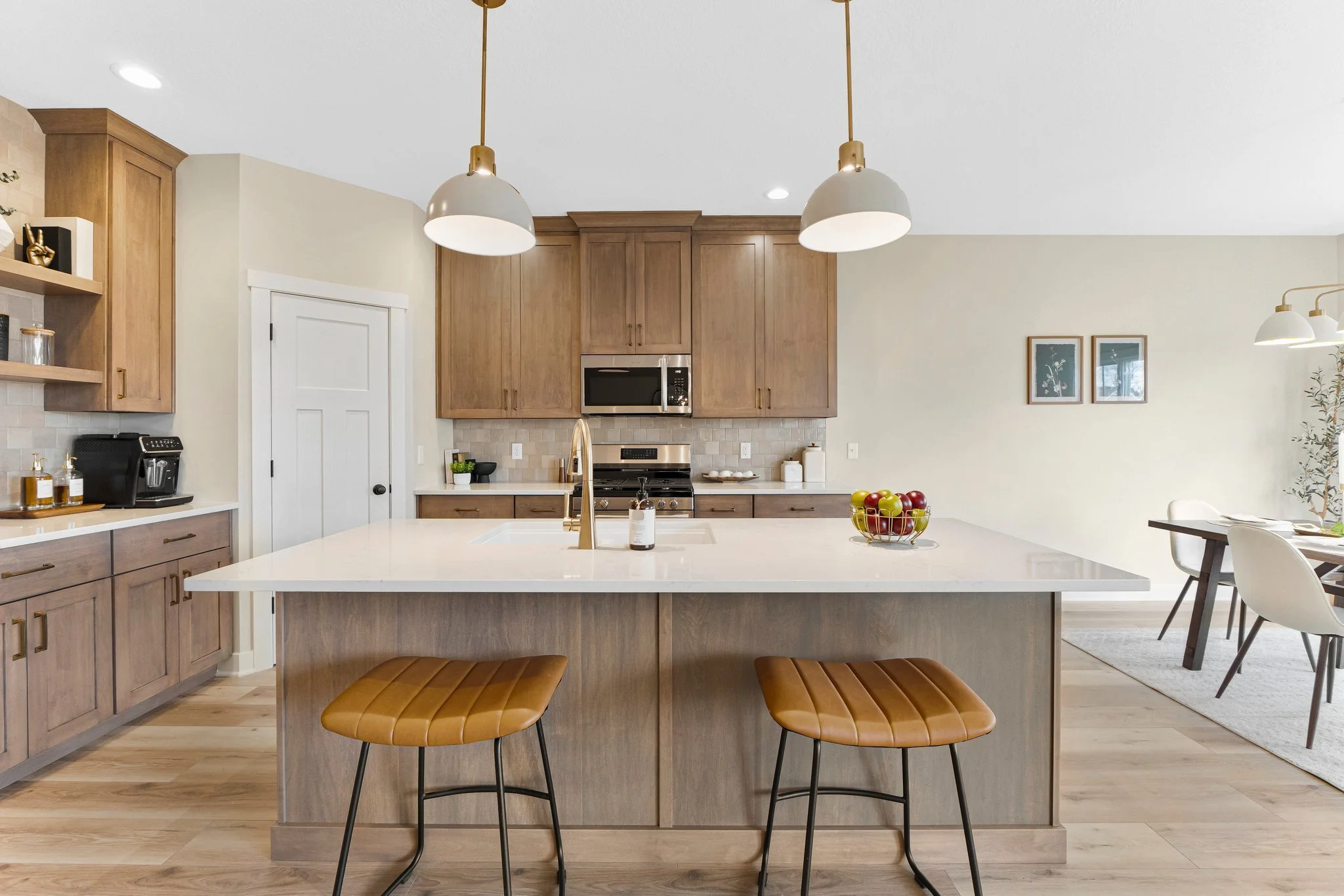 Modern kitchen with a large white island, wooden cabinets, stainless steel appliances, and two brown leather stools at the island.