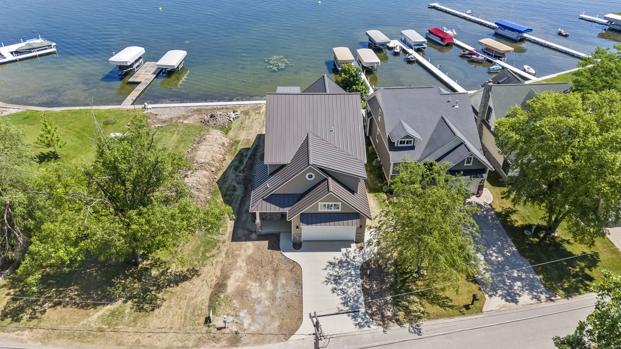 Aerial view of a house under construction near a lake with boat docks and neighboring homes.