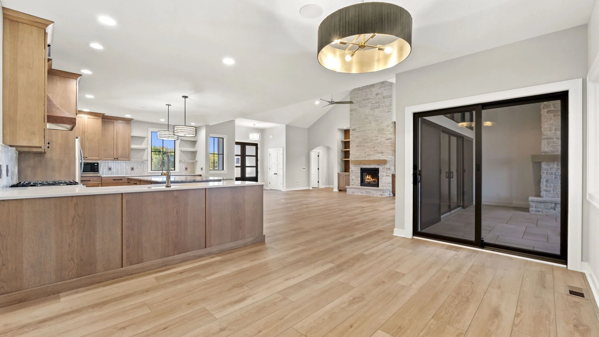 Open concept living room and kitchen with wooden floors, a fireplace with a stone surround, and sliding glass doors leading outside.