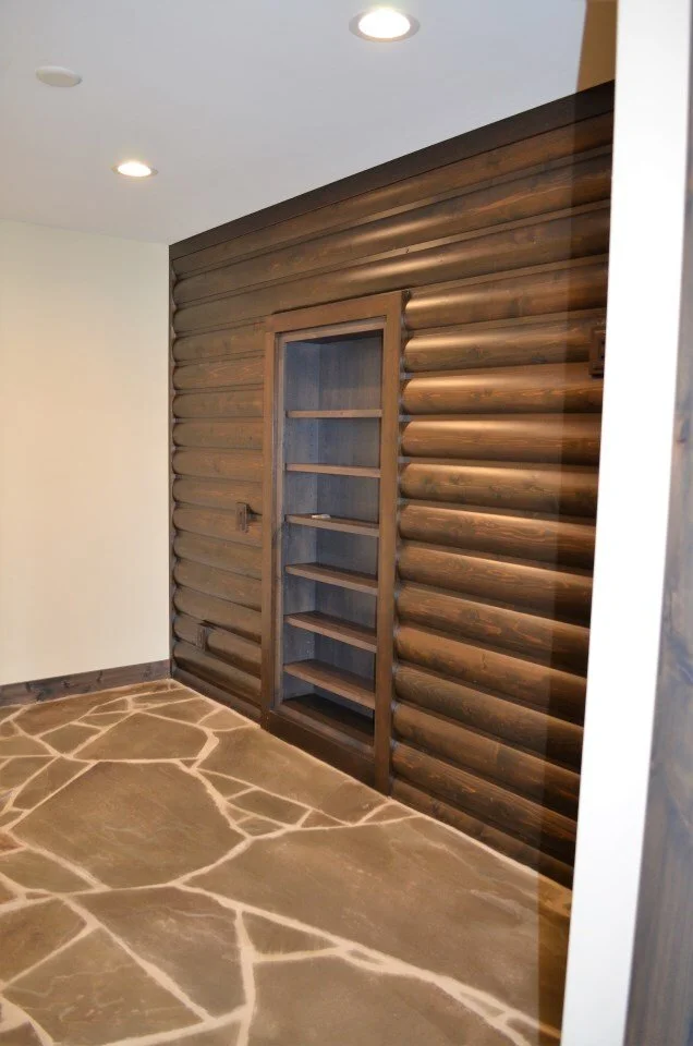 Interior room with a dark wood log-style wall, a built-in open bookshelf in the wall, a white ceiling with recessed lighting, and a natural stone floor with irregular shapes and white grout lines.