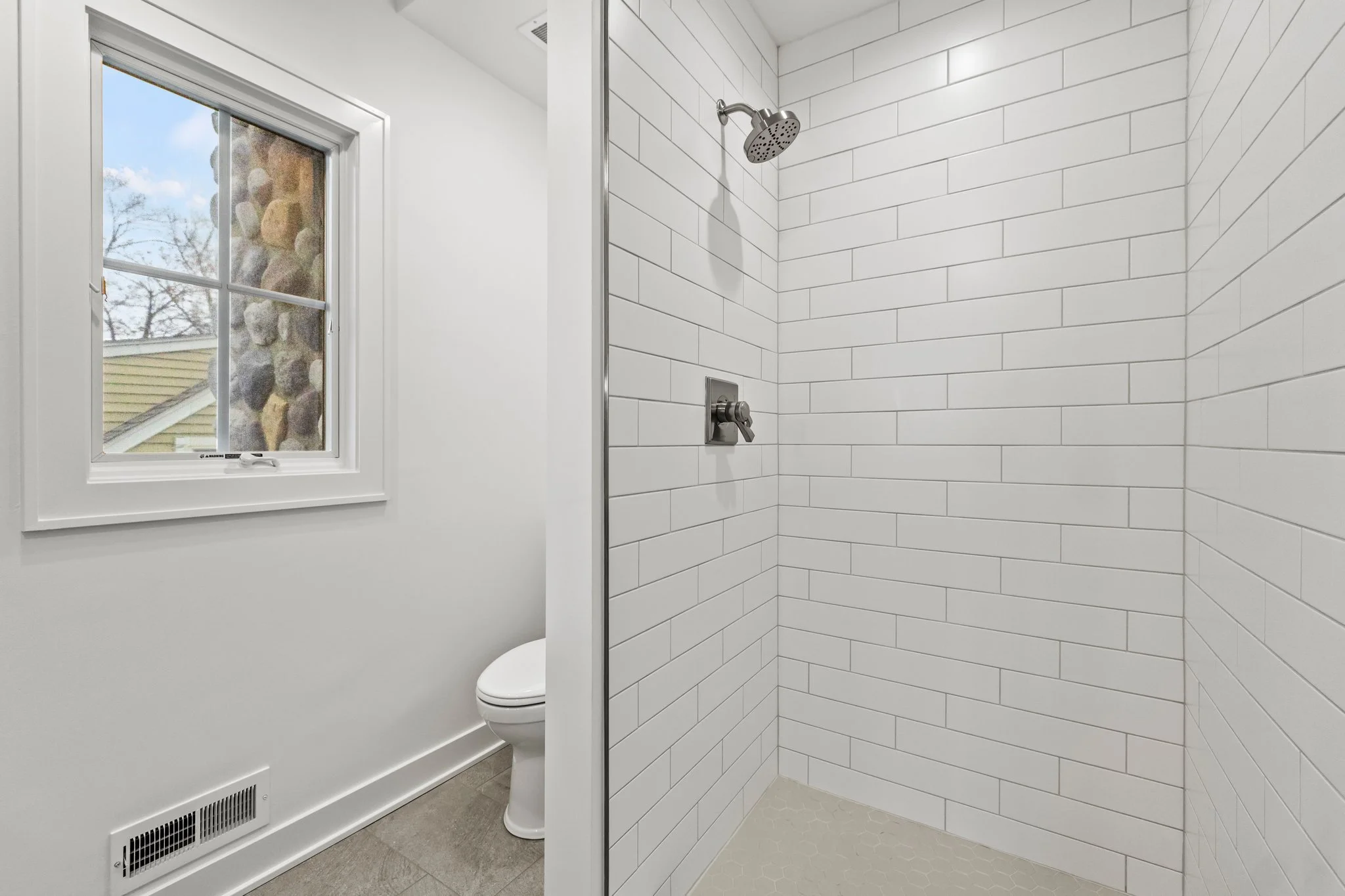 Bathroom with a window, toilet, and a shower with white subway tiles.