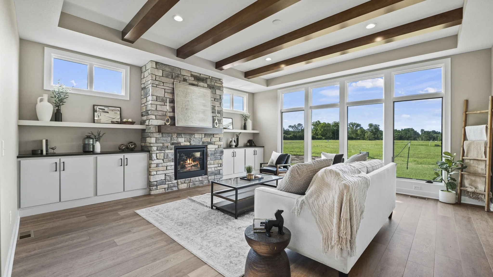 Bright living room with large windows, stone fireplace, white sofa, black chairs, glass coffee table, and decor on shelves.