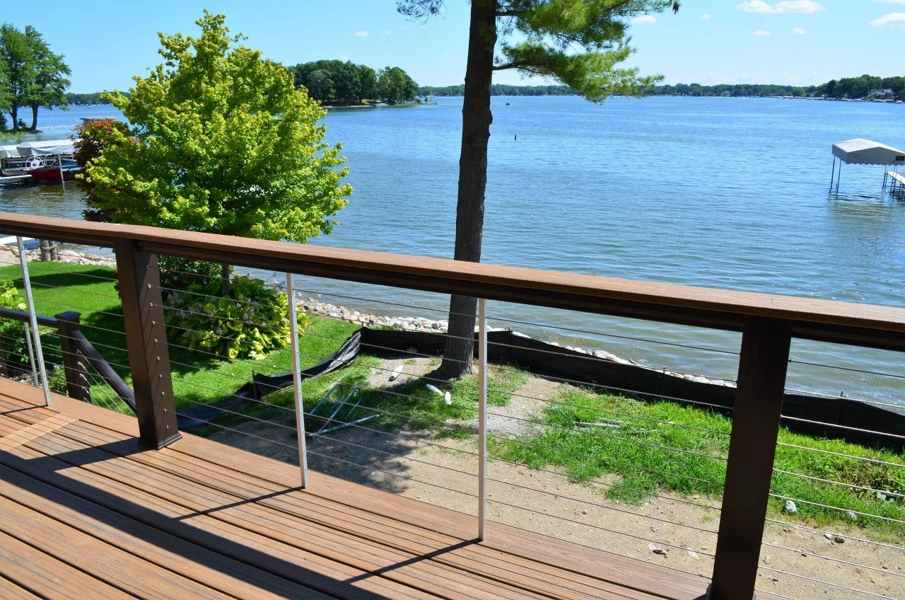View from a wooden deck overlooking a lake with trees, a boat dock, and calm water on a sunny day.