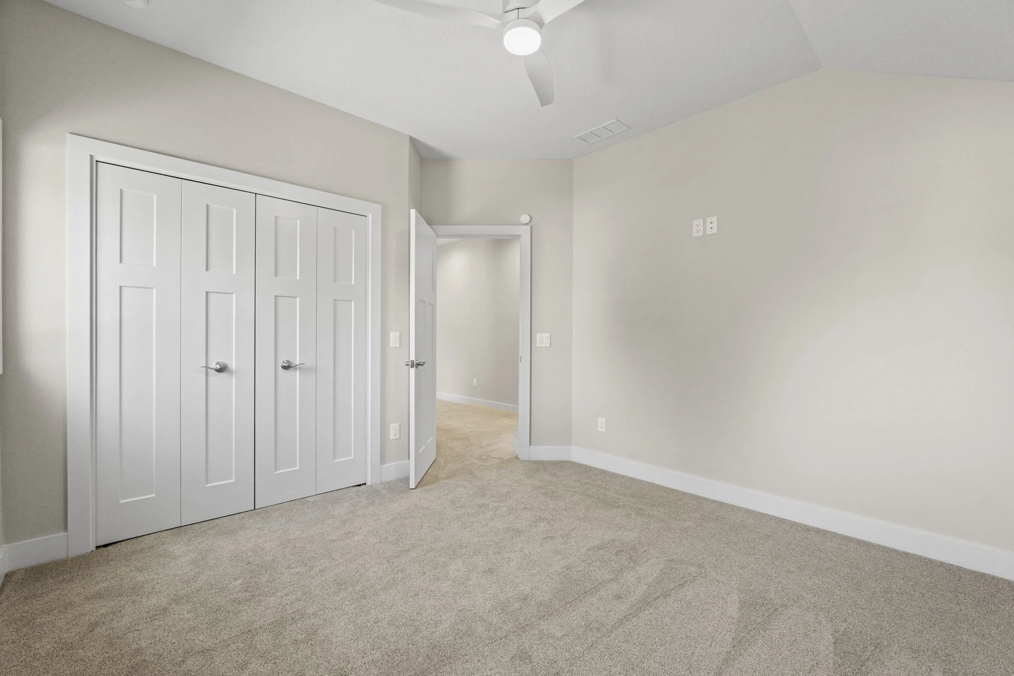 Empty beige carpeted bedroom with white doors, ceiling fan, and light-colored walls.