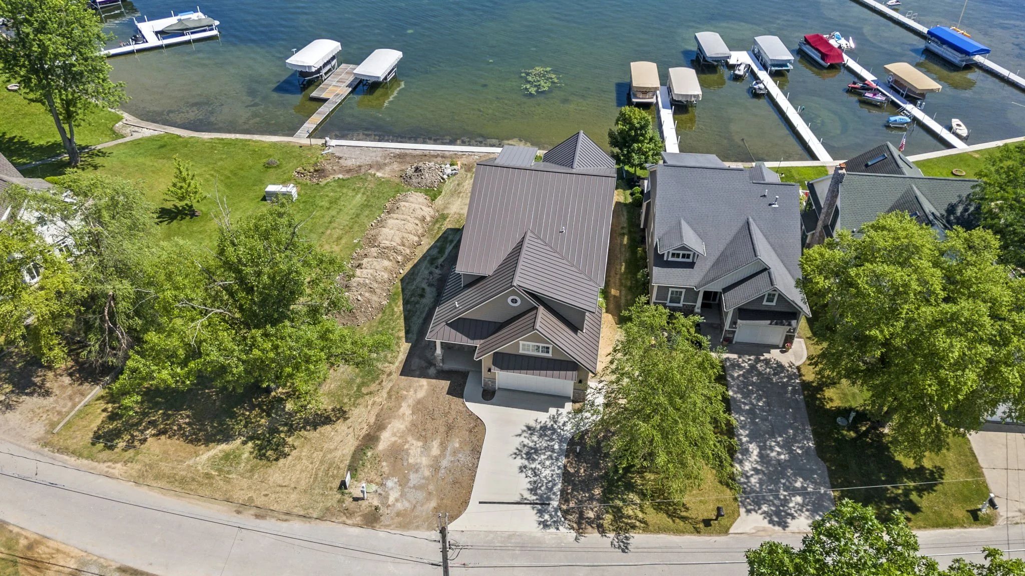 Aerial view of a residential waterfront property with a house, boat docks, and several boats on the water. Trees and lawns surround the house, with a driveway leading to the street.