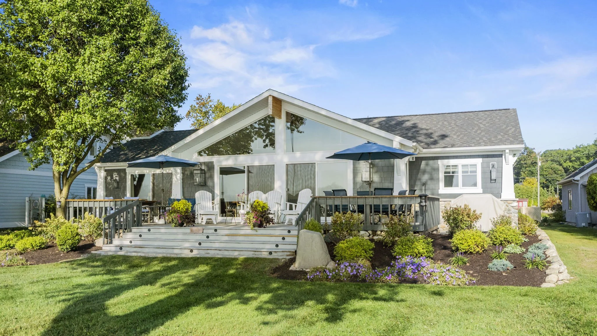 Backyard of a house with a deck, outdoor furniture, and a landscaped garden with bushes and flowers.