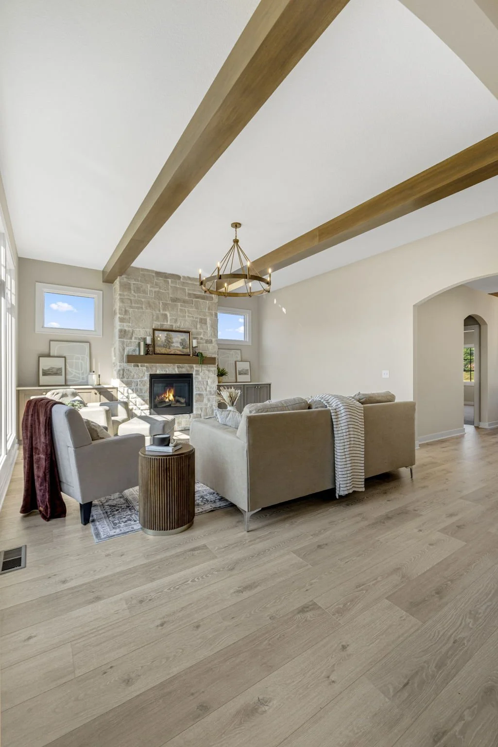 Bright living room with beige sofa, armchair, stone fireplace, and wooden beams on ceiling.
