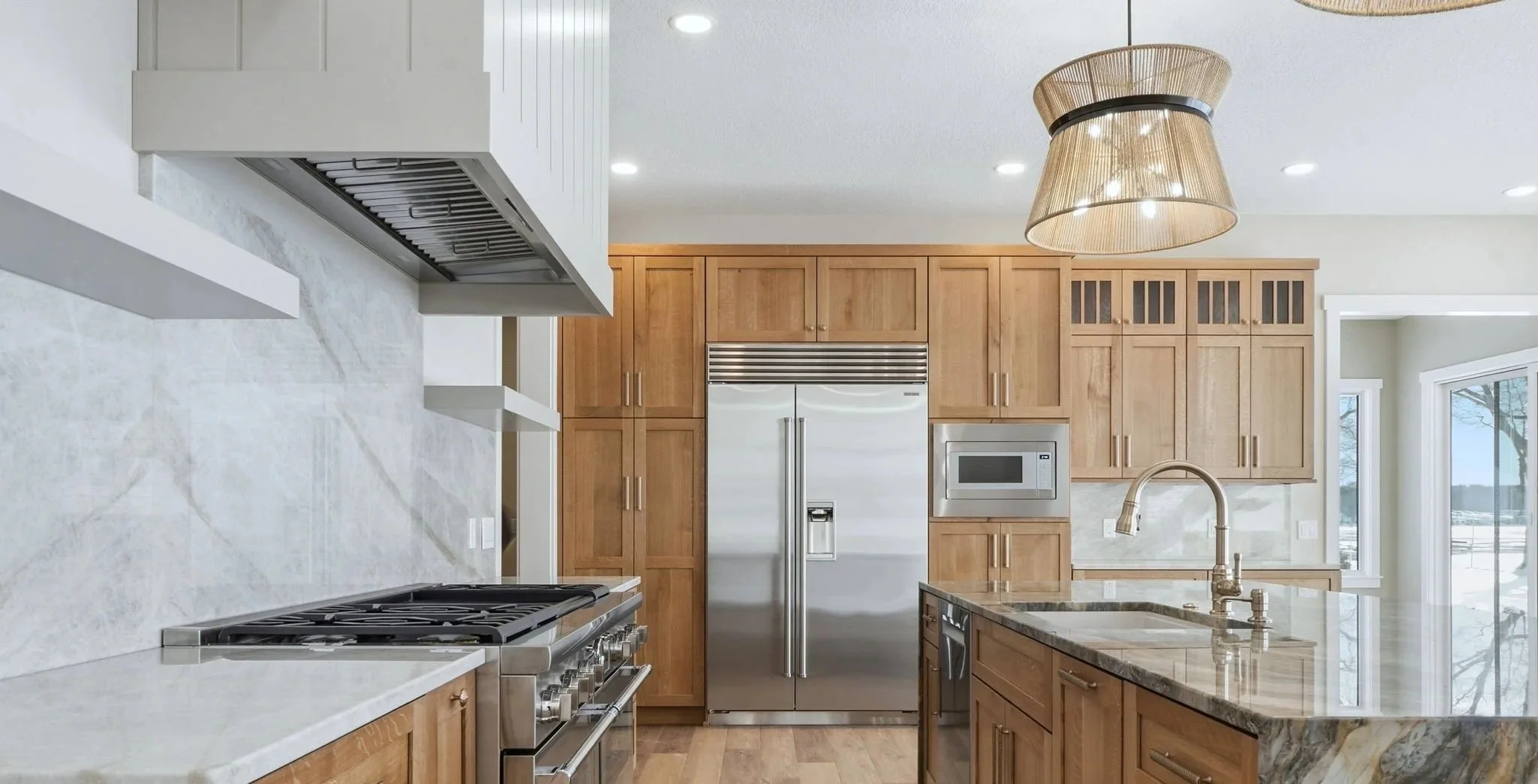 Modern kitchen with wooden cabinets, white marble countertops, stainless steel appliances, large window, and a unique pendant light
