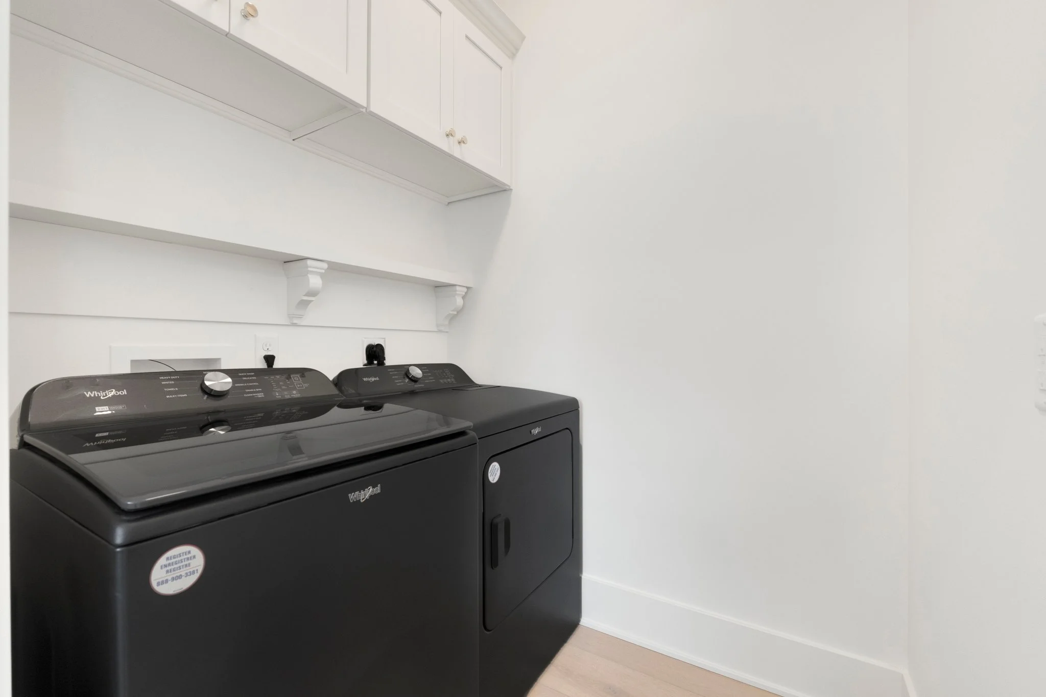 A black Whirlpool washer and dryer set in a laundry room with white walls and light wood flooring.
