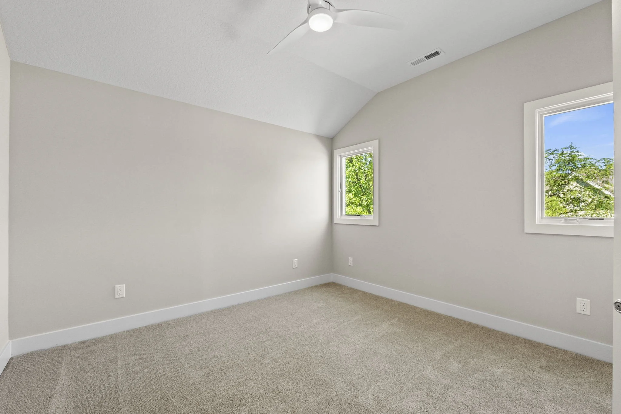 Empty room with two windows, beige carpet, white walls, ceiling fan, and white baseboards.