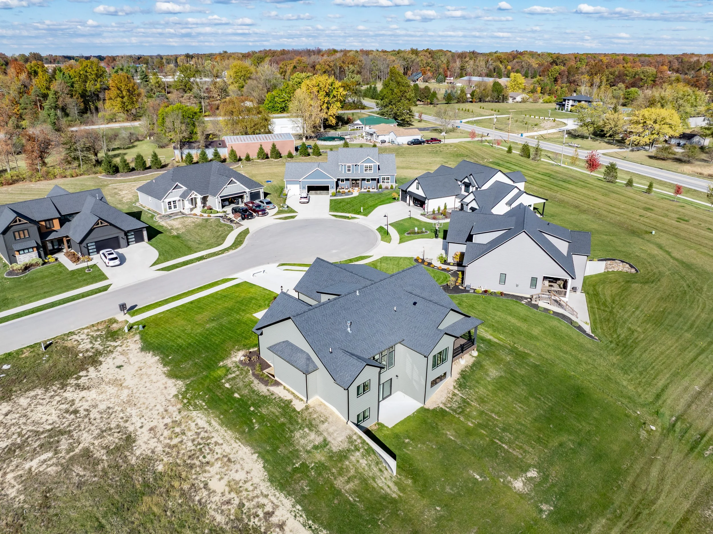 Aerial view of a suburban neighborhood with multiple modern houses, manicured lawns, and trees in the background during daytime.