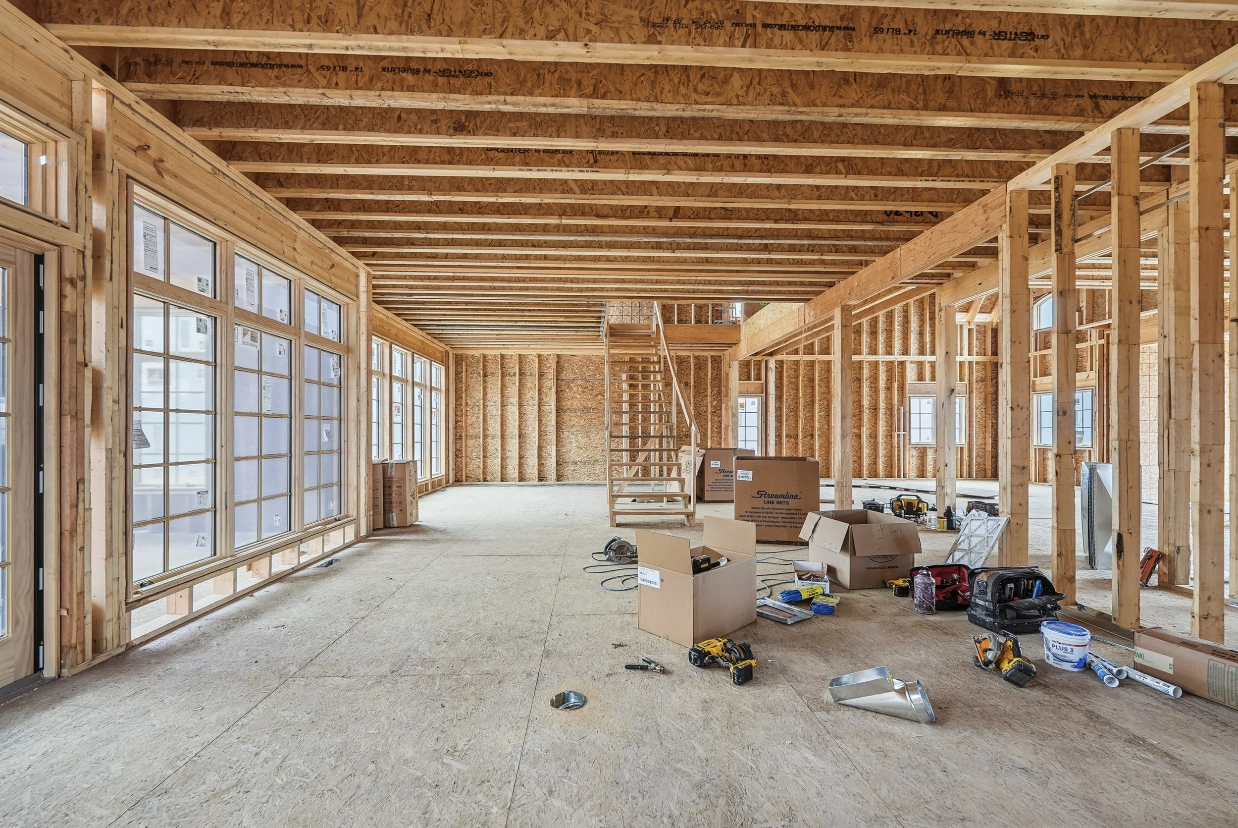 Interior of a house under construction with exposed wooden framing, unfinished walls, and construction tools and boxes on the floor.