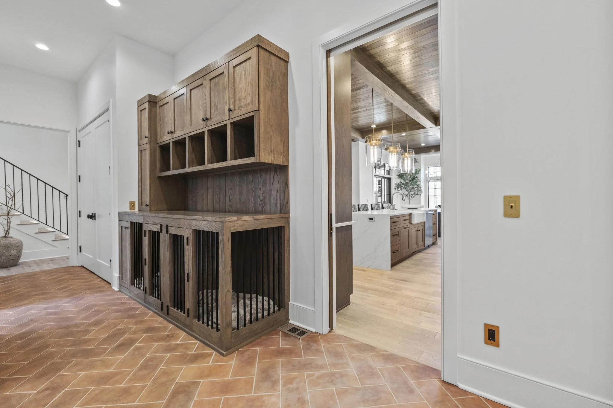 Living area with terracotta tile flooring, white walls, a built-in wooden cabinet, sliding barn door, and an open kitchen with wooden cabinets and pendant lights.