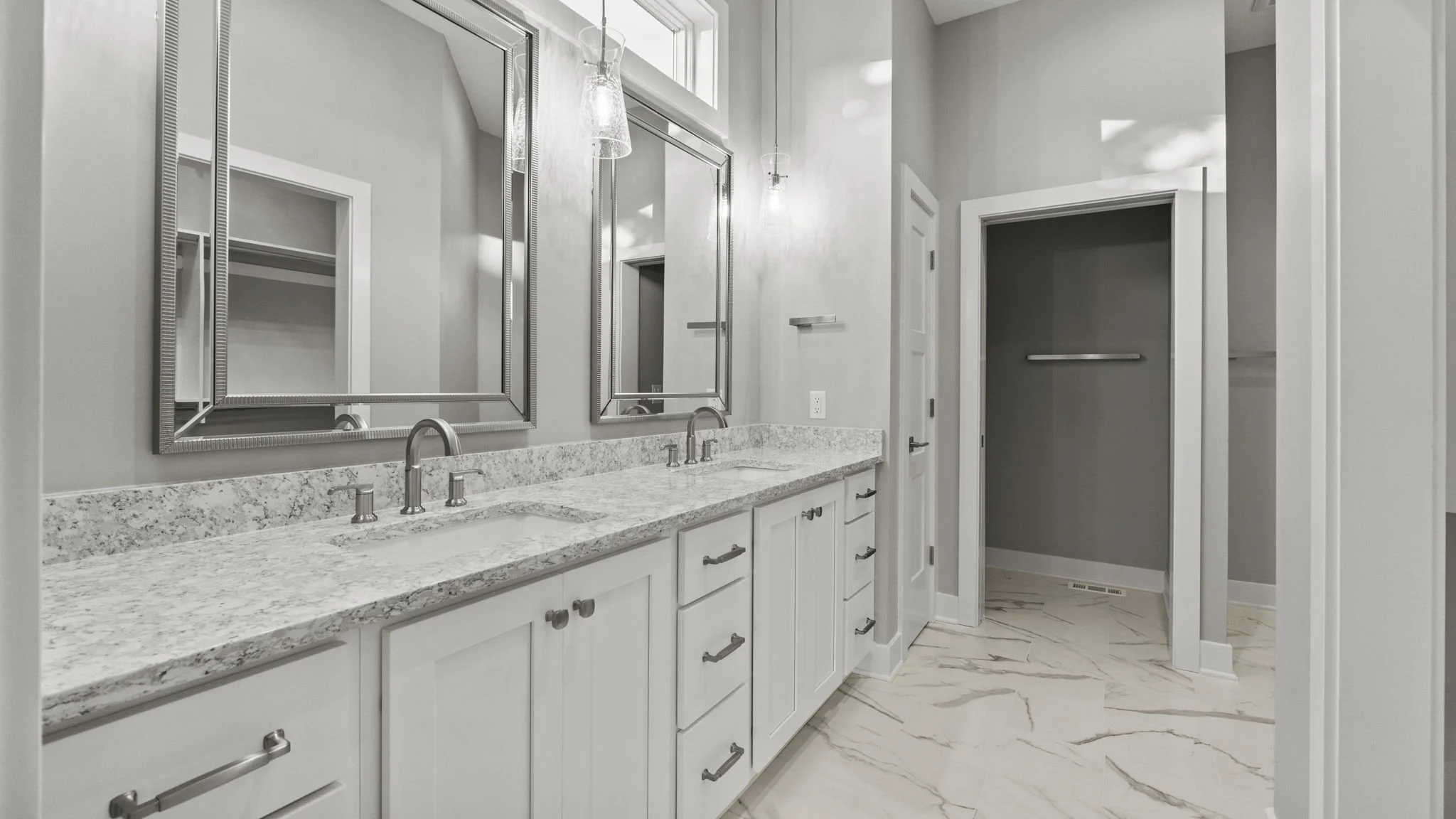 Modern bathroom with double vanity, marble countertop, two mirrors, and a walk-in closet.