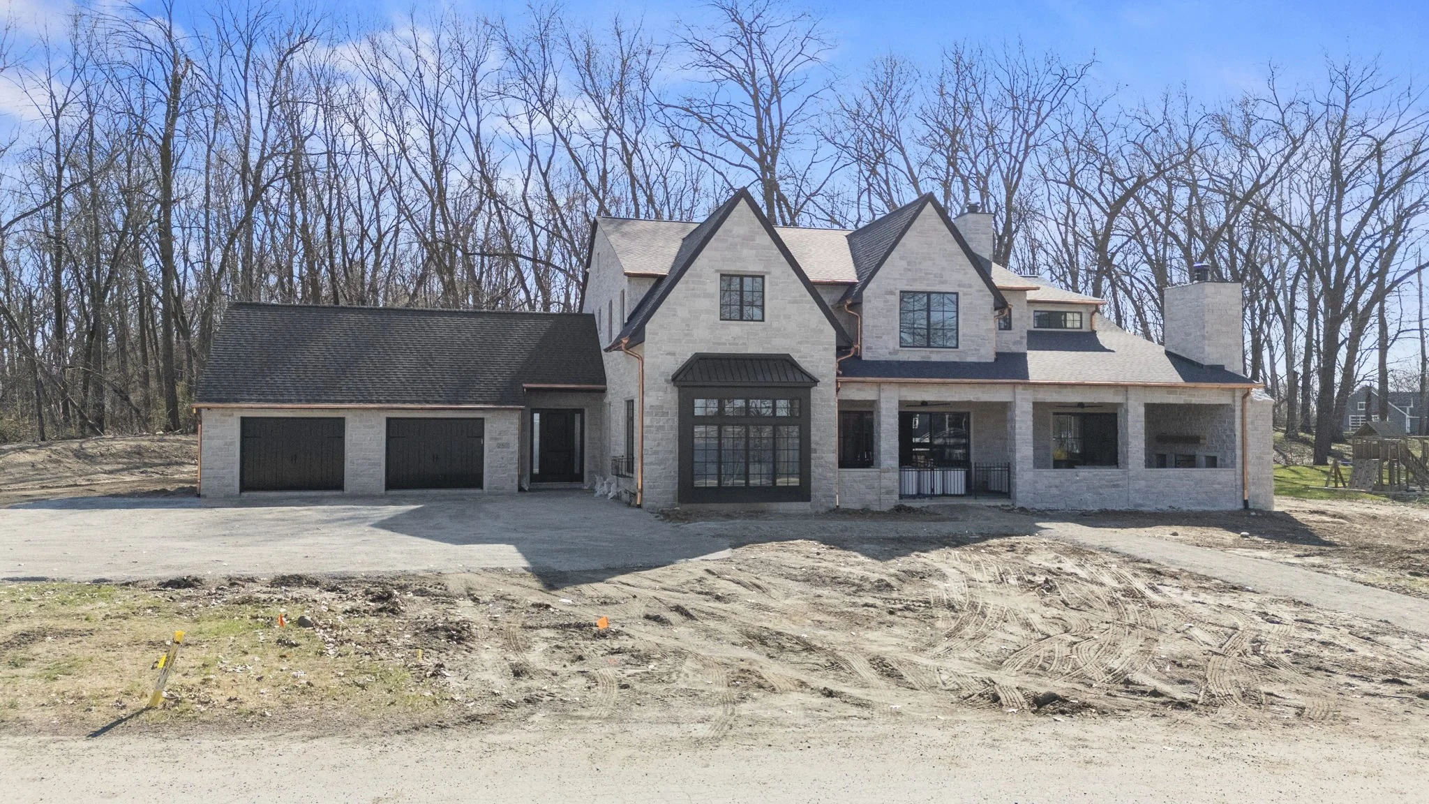 Front of a newly constructed two-story house with a garage, surrounded by bare trees, under a blue sky.