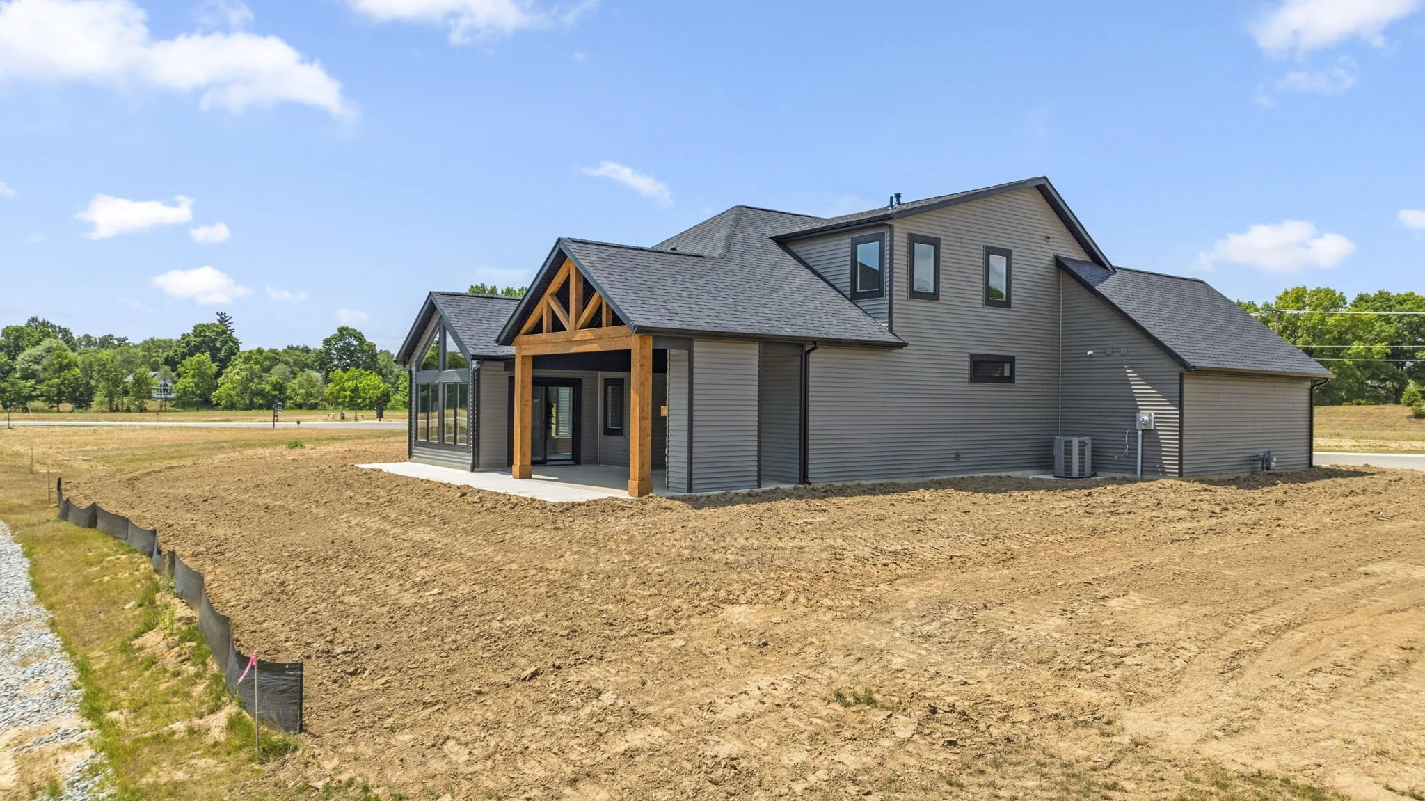 Newly built gray house with black roof and wood trim, sitting on a landscaped lot under a blue sky with clouds.