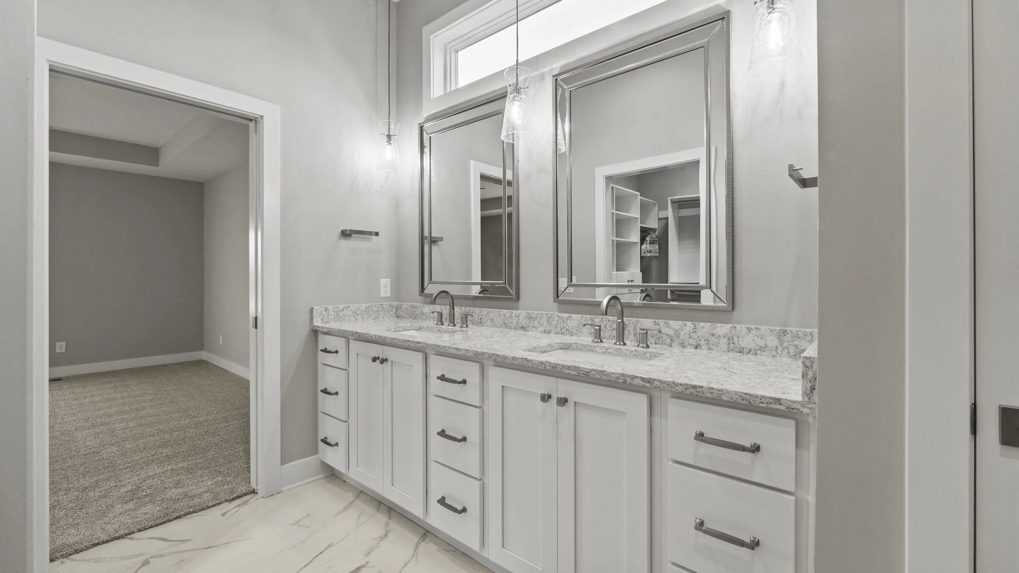 Modern bathroom vanity with white cabinets, granite countertop, two sinks, two mirrors, and pendant lighting, with an adjacent walk-in closet.