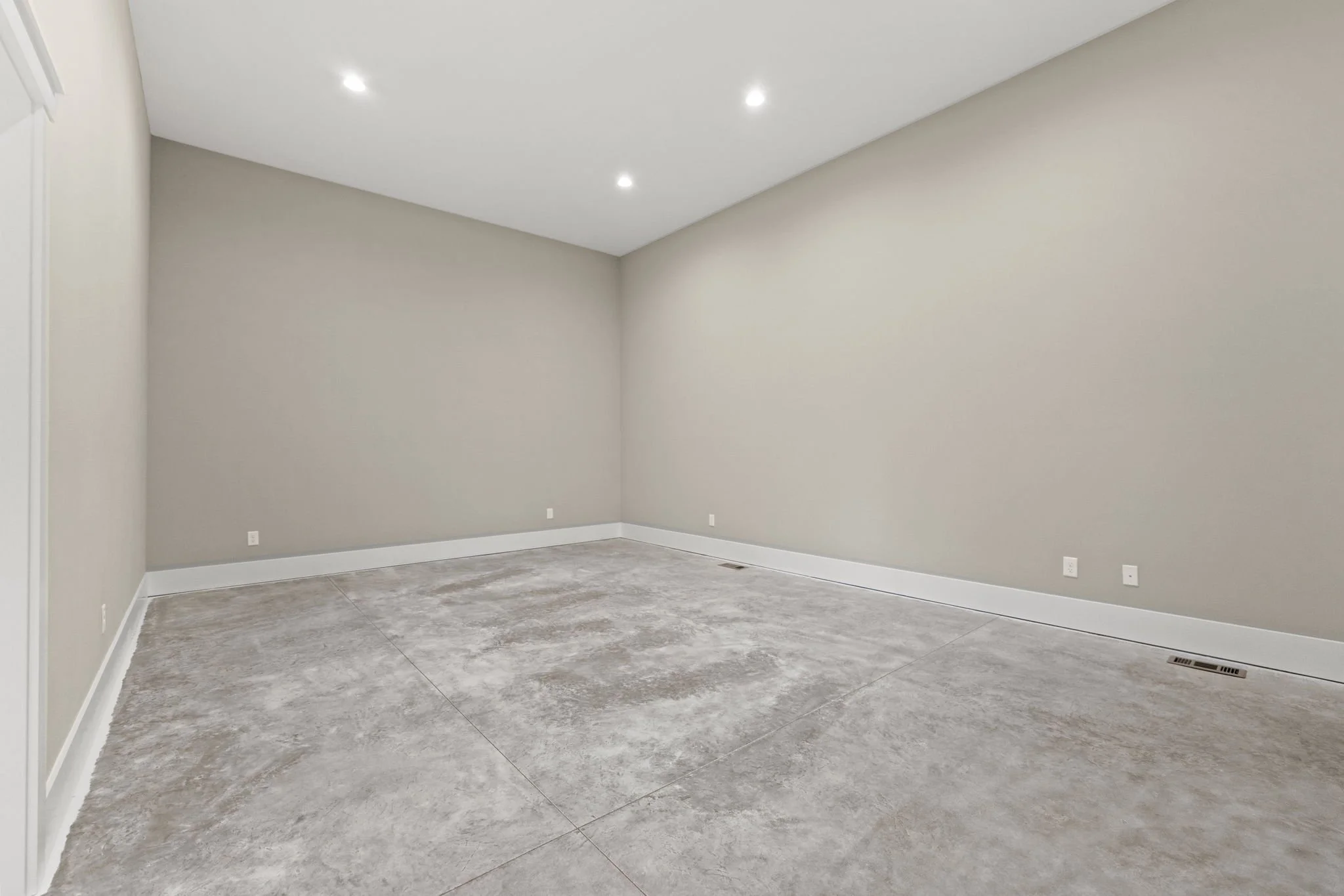 Empty room with beige walls, gray concrete floor, white baseboards, and recessed ceiling lights.