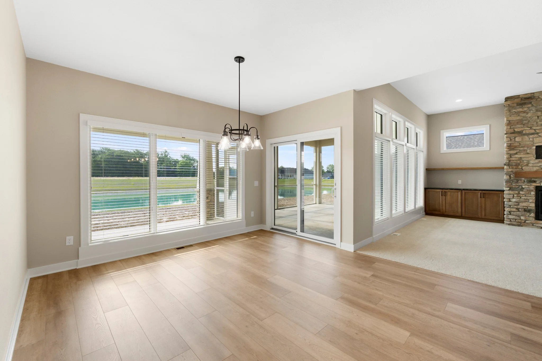 Empty living room with hardwood floors, large windows, a sliding glass door, and a view of a backyard with a pool.