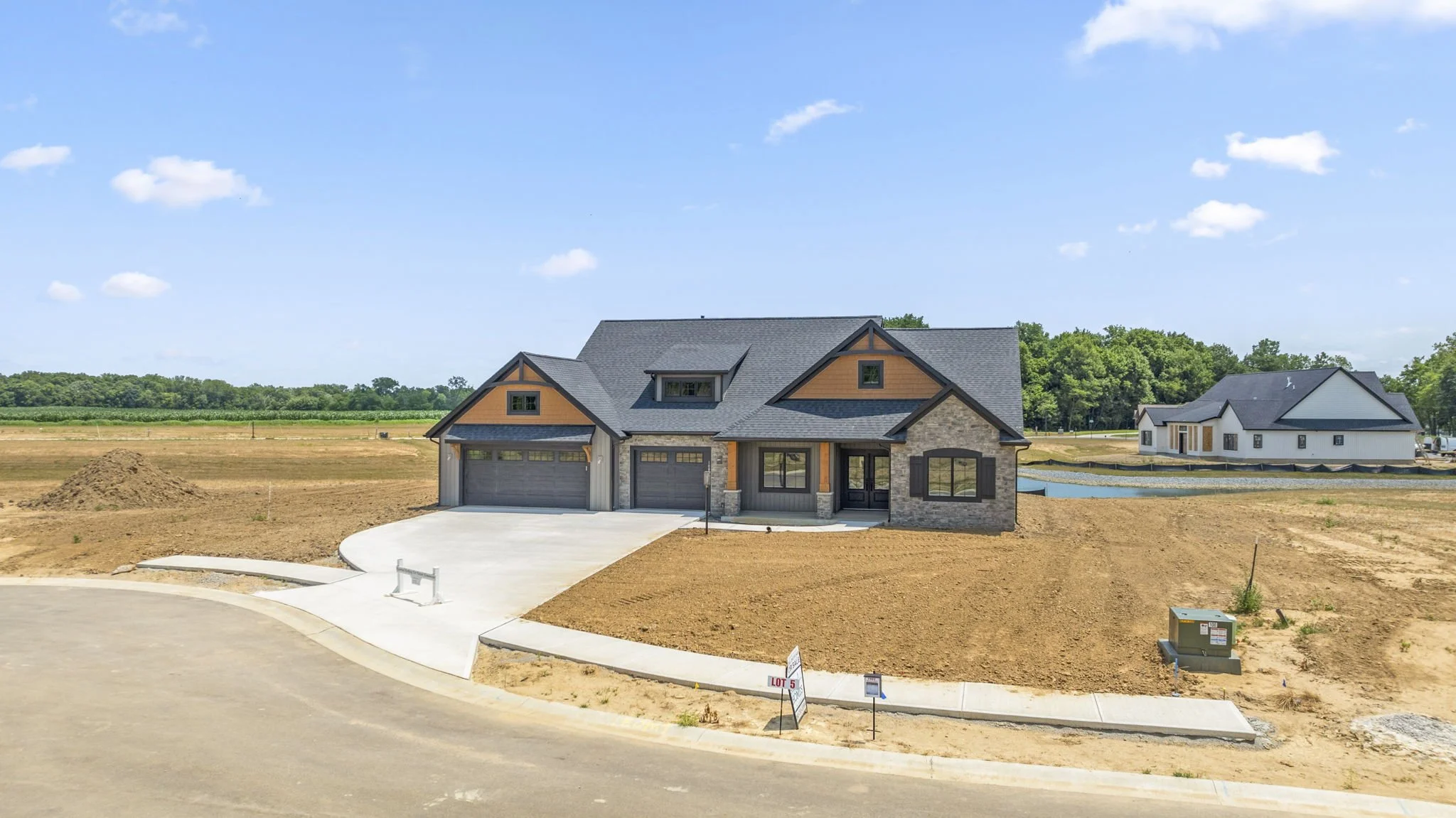 Newly constructed house with three garage doors, situated on a lot with freshly tilled soil, under a bright blue sky with some clouds.