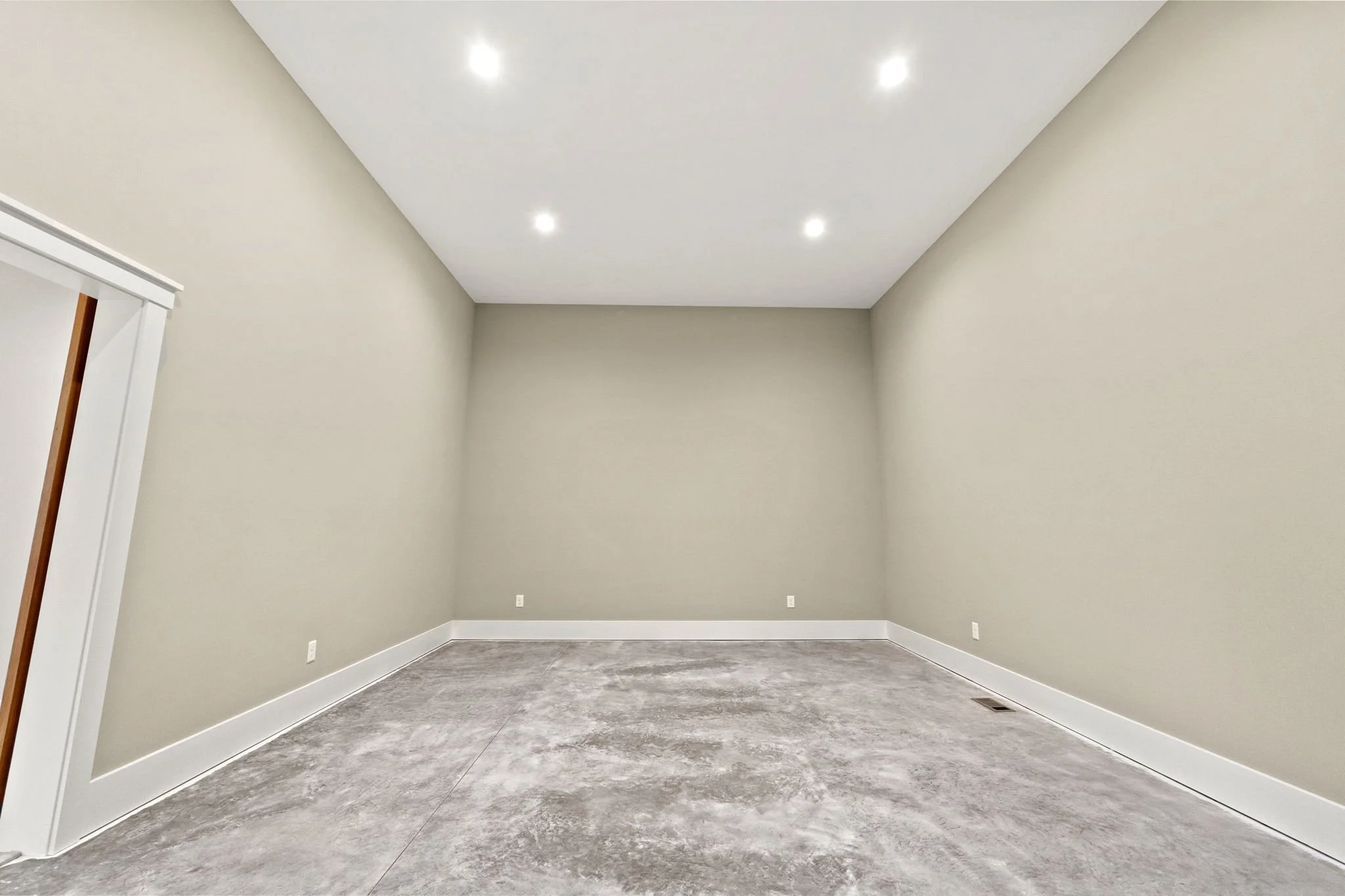Empty room with beige walls, white trim, gray floor, and ceiling lights.