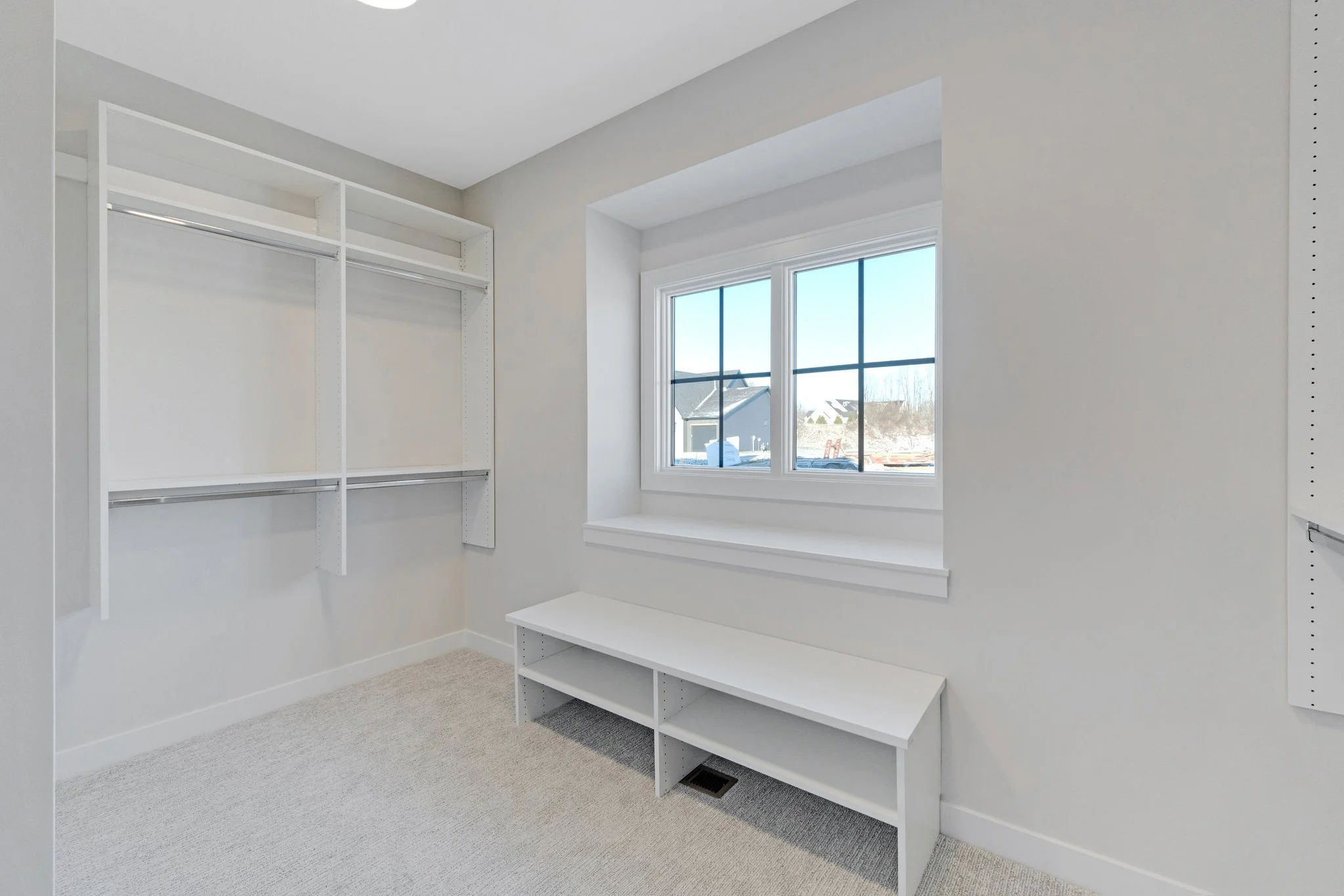 Empty walk-in closet with white shelving, a bench near a window, and another shelving unit on the wall.