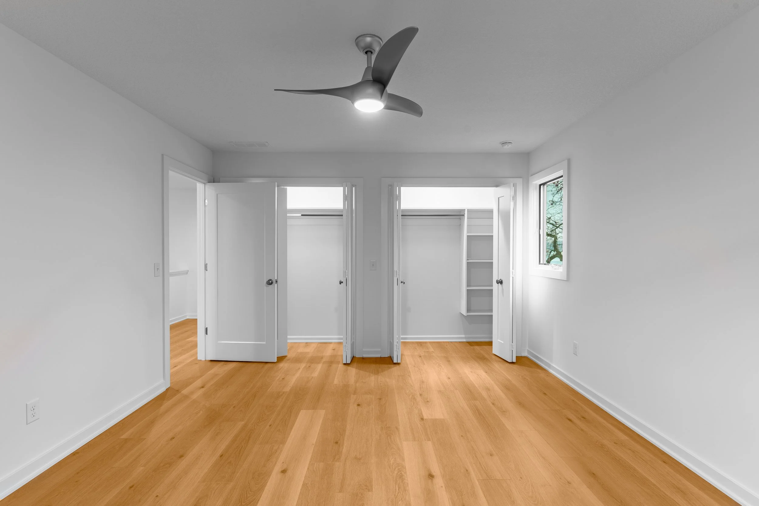 Empty bedroom with hardwood floors, white walls, an open closet with double doors, and a ceiling fan with a light.